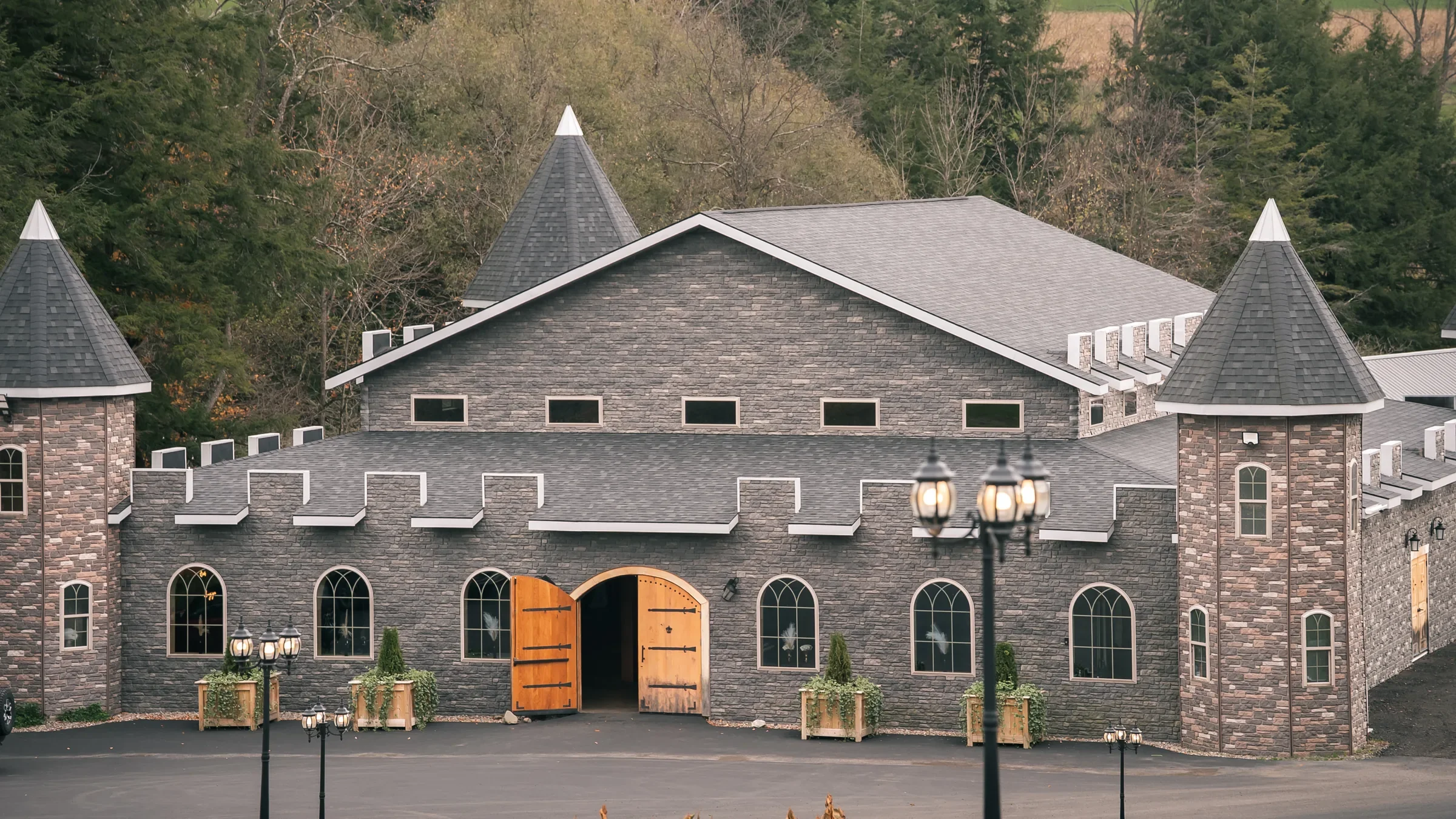 Front exterior of Stoney Creek Castle with gray stone walls, turrets, arched windows, and open wooden doors in Earlville, New York