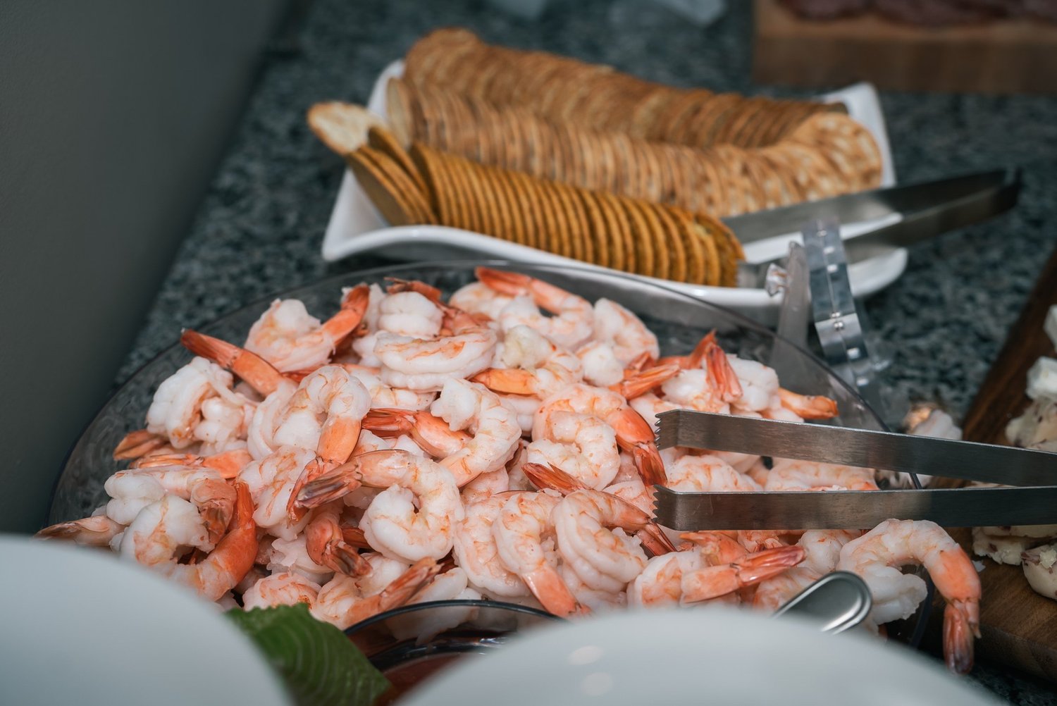 A platter of shrimp on ice beside crackers at the cocktail hour