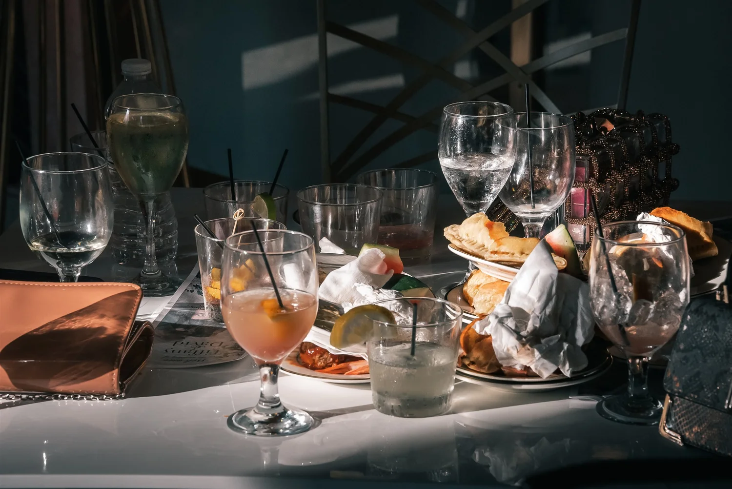 Sunlight falls across wine glasses and green-accented place settings beside a window.