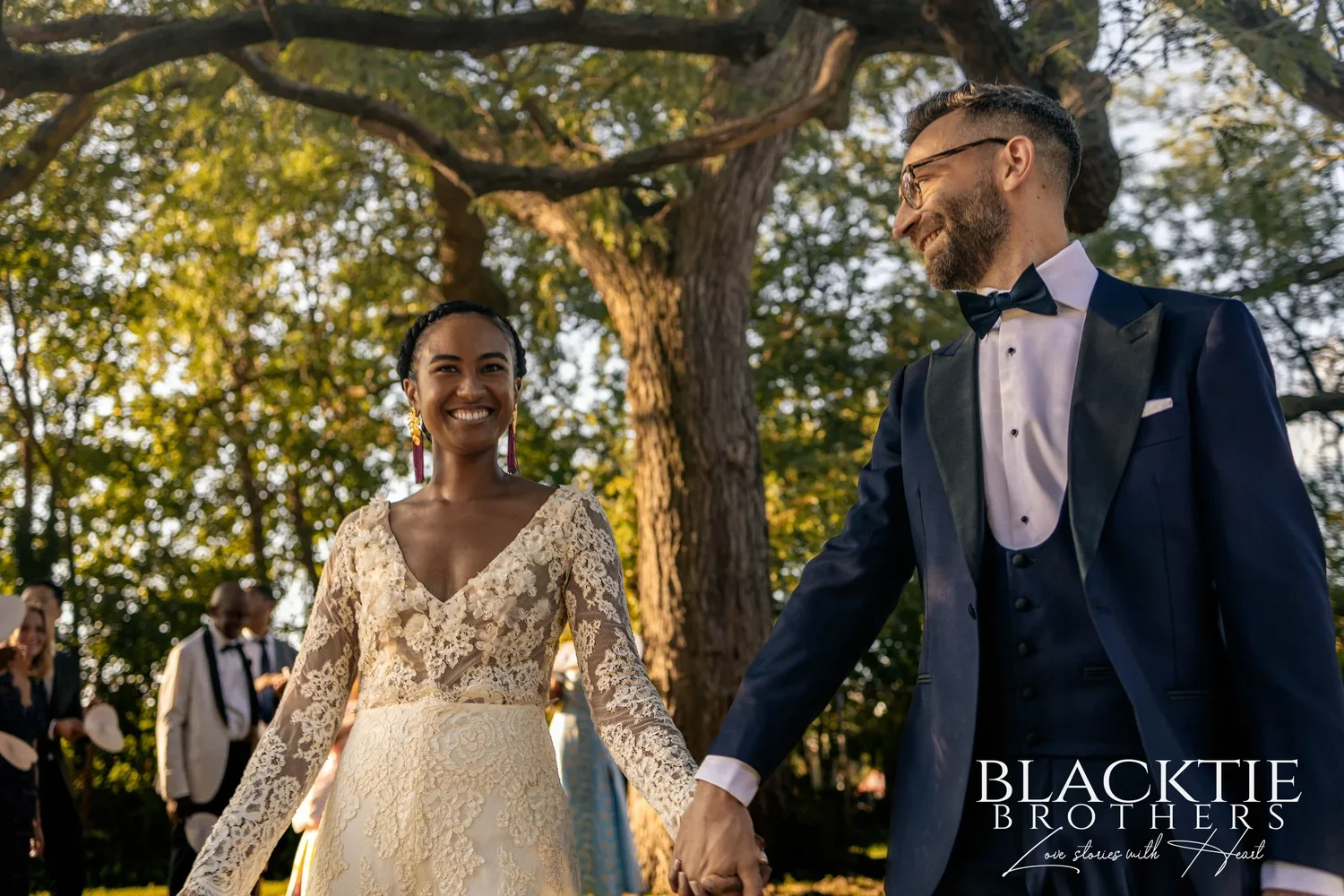 Ciara and Drew walking back up the aisle hand in hand, laughing under the spreading branches of the park trees