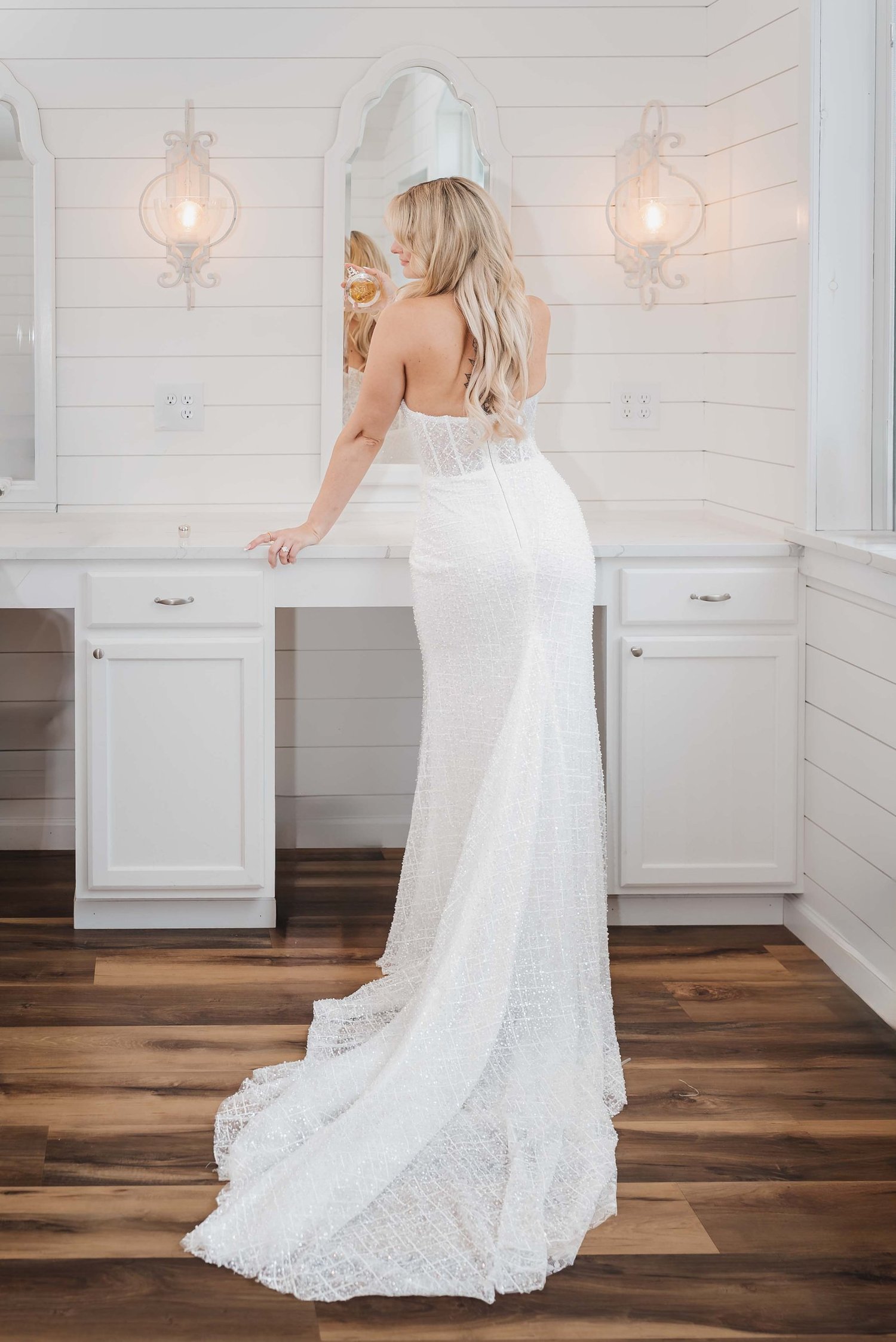 Kari stands at a white vanity with a perfume bottle, the long train of her beaded gown spread across the wooden floor.