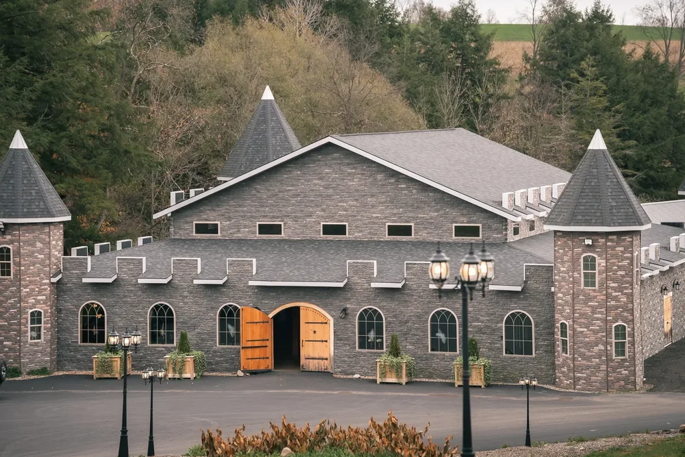 Front exterior of Stoney Creek Castle with gray stone walls, turrets, arched windows, and open wooden doors in Earlville, New York