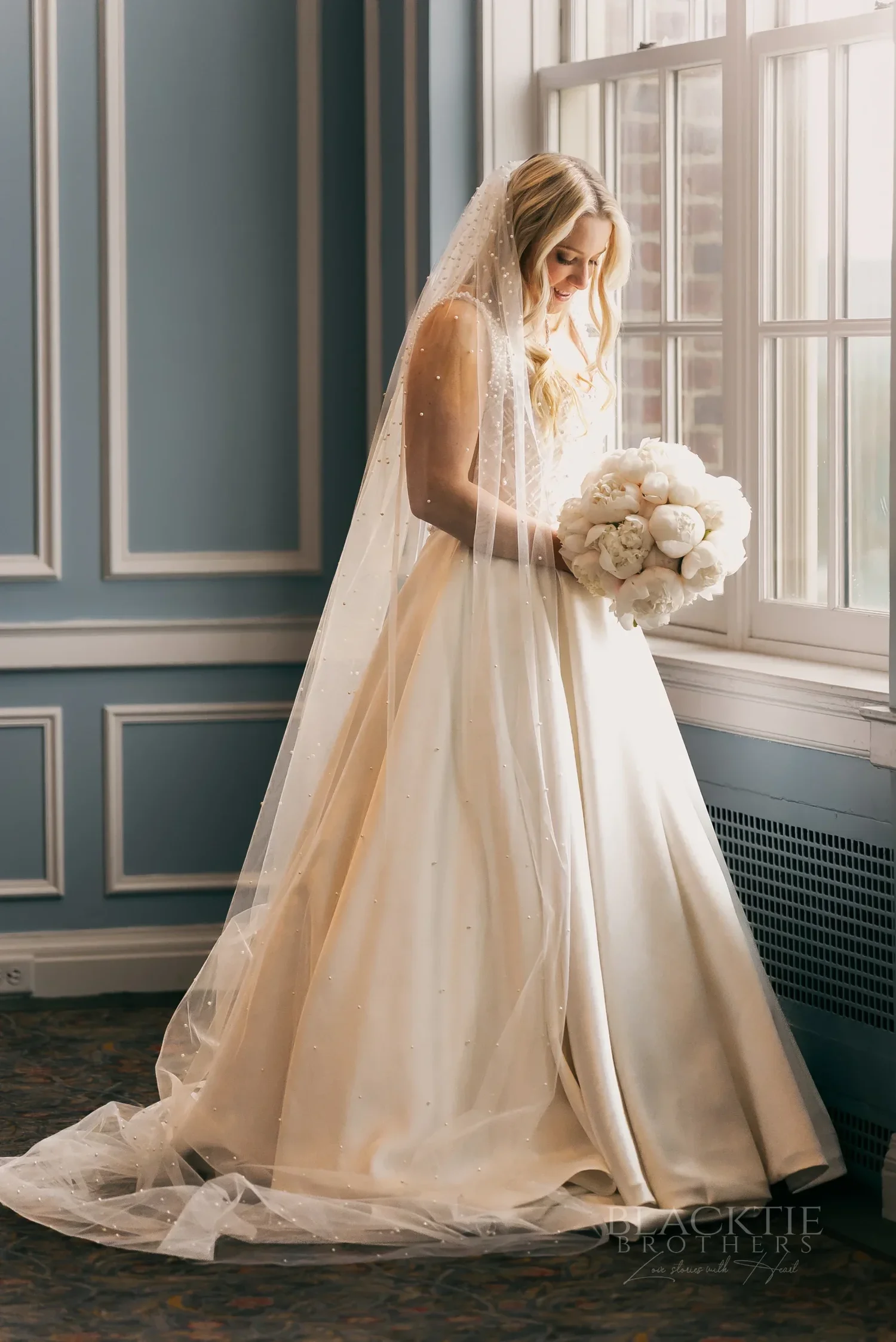 Bridal portrait of Catie holding white roses by the window at Marriott Syracuse Downtown