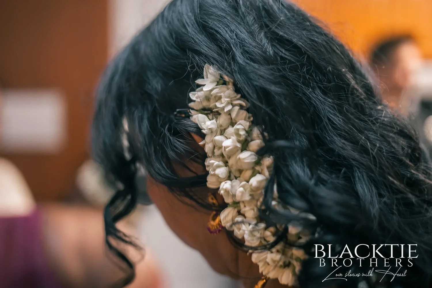 Strands of white flower buds pinned into long, curled dark hair, seen from behind