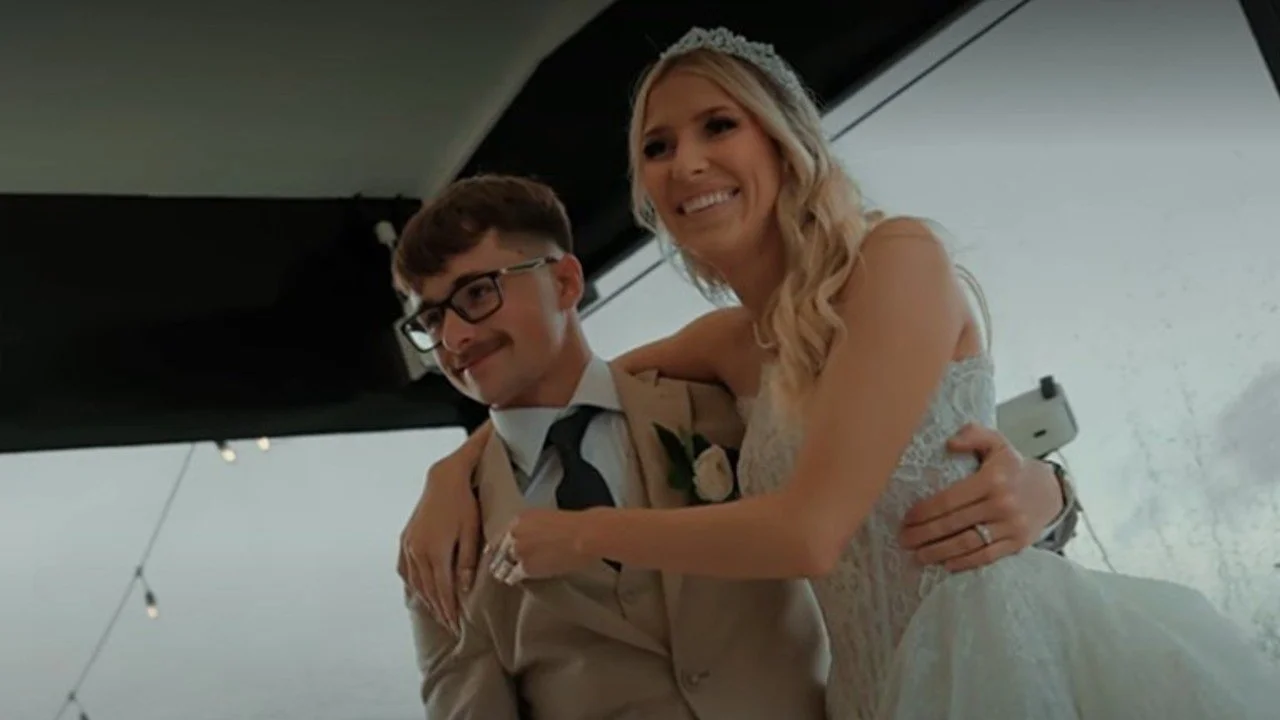 Callie, in her tiara, hugging Jaycob from behind under the pavilion roof, both of them smiling