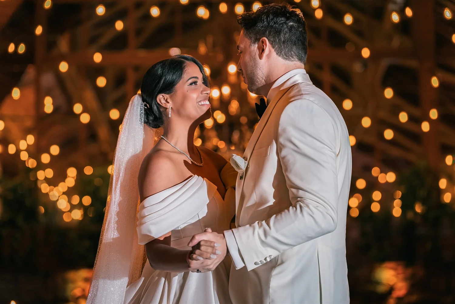 Patricia smiles at Joshua as they hold hands beneath the warm lights in The Somerley reception room.