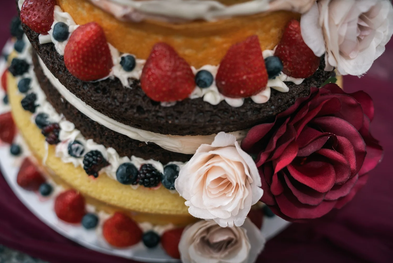 Close-up of a naked wedding cake layered with strawberries, blueberries and roses
