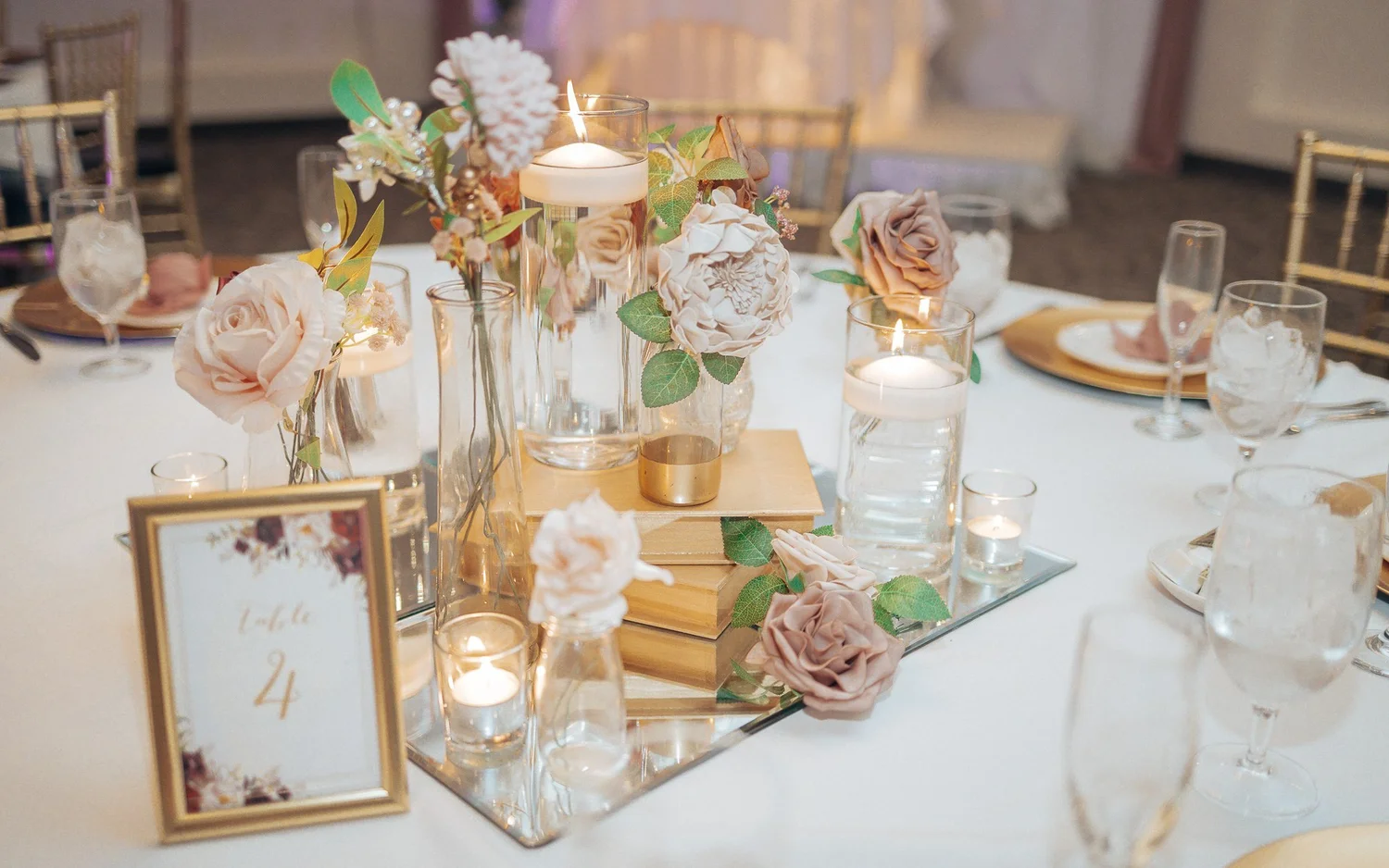 A table centerpiece of blush roses, candles and a framed table number on a mirrored tray
