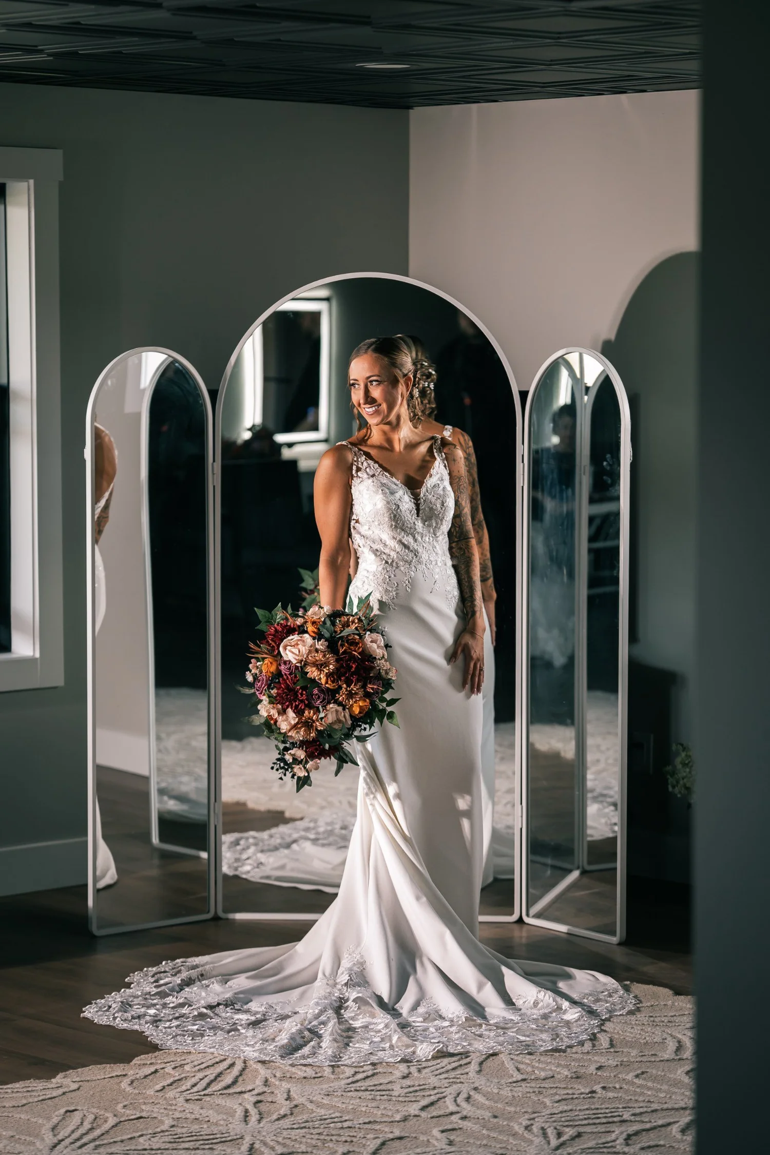 Heather in her wedding gown standing between tall arched mirrors, holding her bouquet