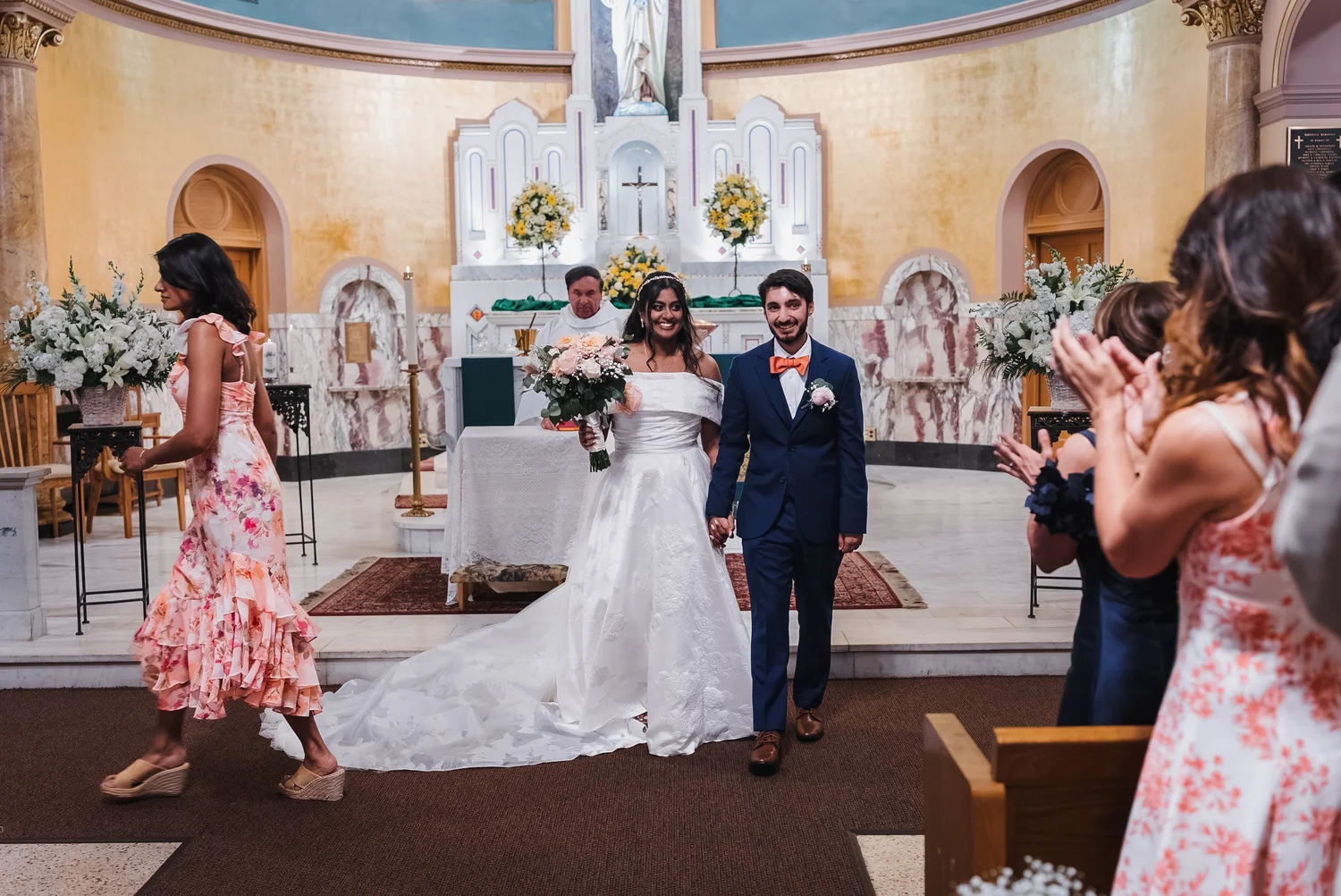 Natalia and Ansel walking back up the aisle as guests clap, with the church altar behind them