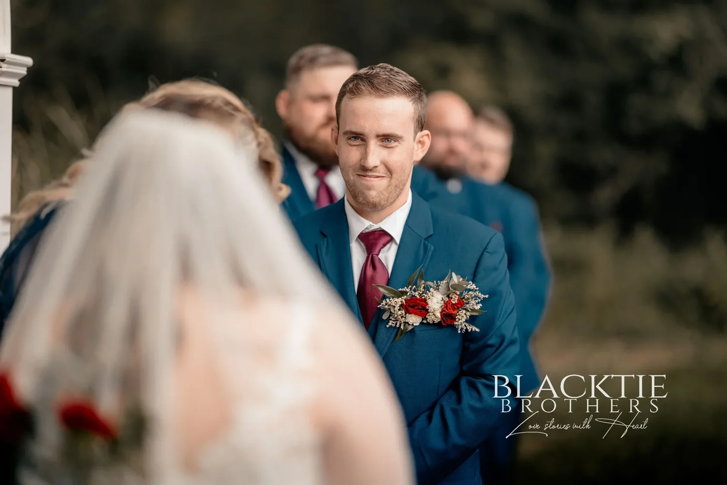 Jared at the arbor smiling as Jennifer approaches, her veil soft and out of focus in the foreground