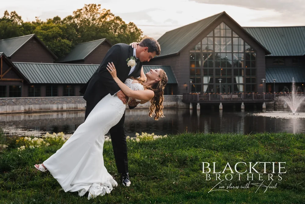 A couple on the far bank of the pond at Allyn Lodge in Skaneateles Falls, New York, with the timber lodge and its fountain behind them at sunset