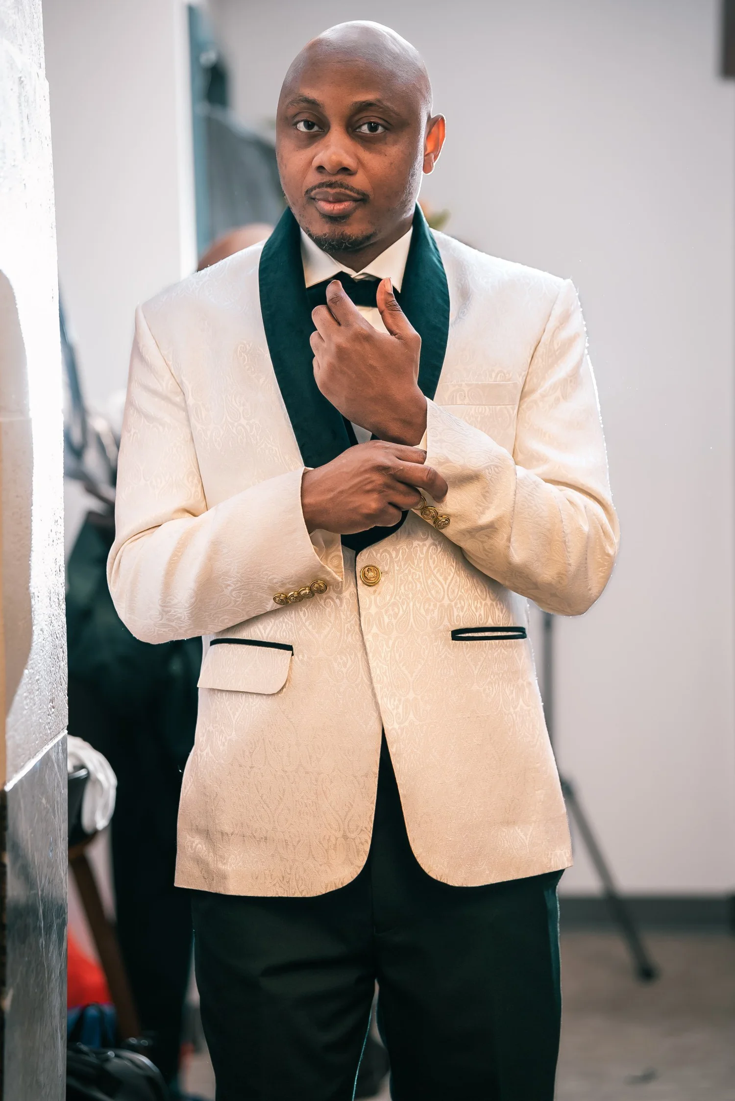 David in his ivory jacket with green velvet lapels and a black bow tie, adjusting his cuffs before the ceremony.