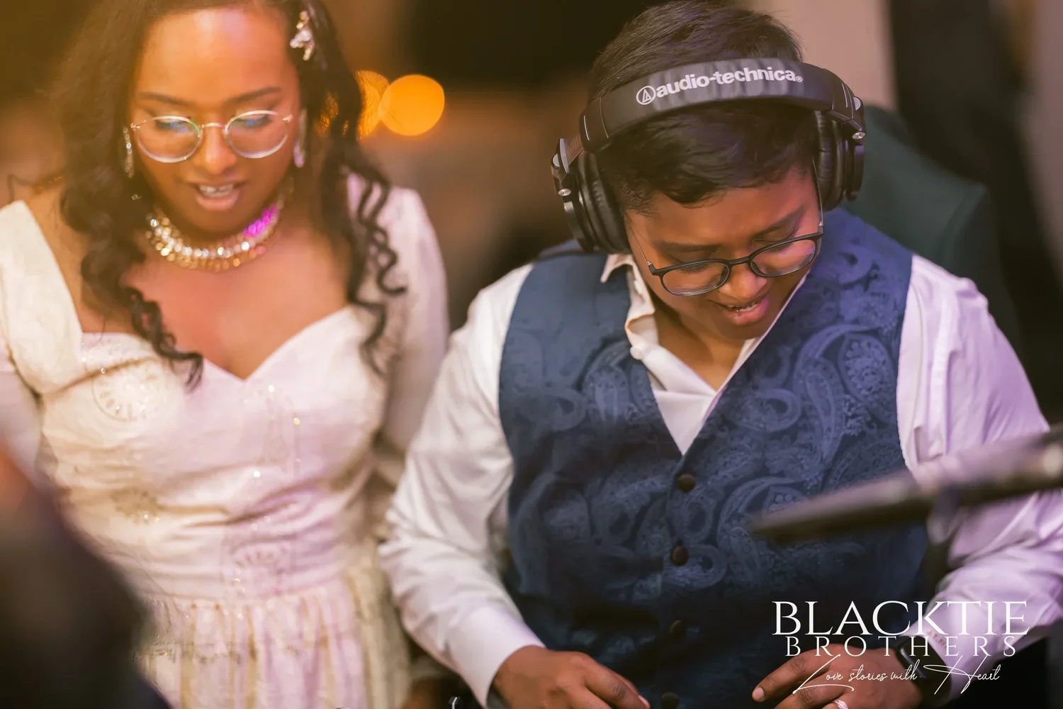 Hima and Alina laughing together at the DJ booth, one wearing headphones, one in a white evening dress