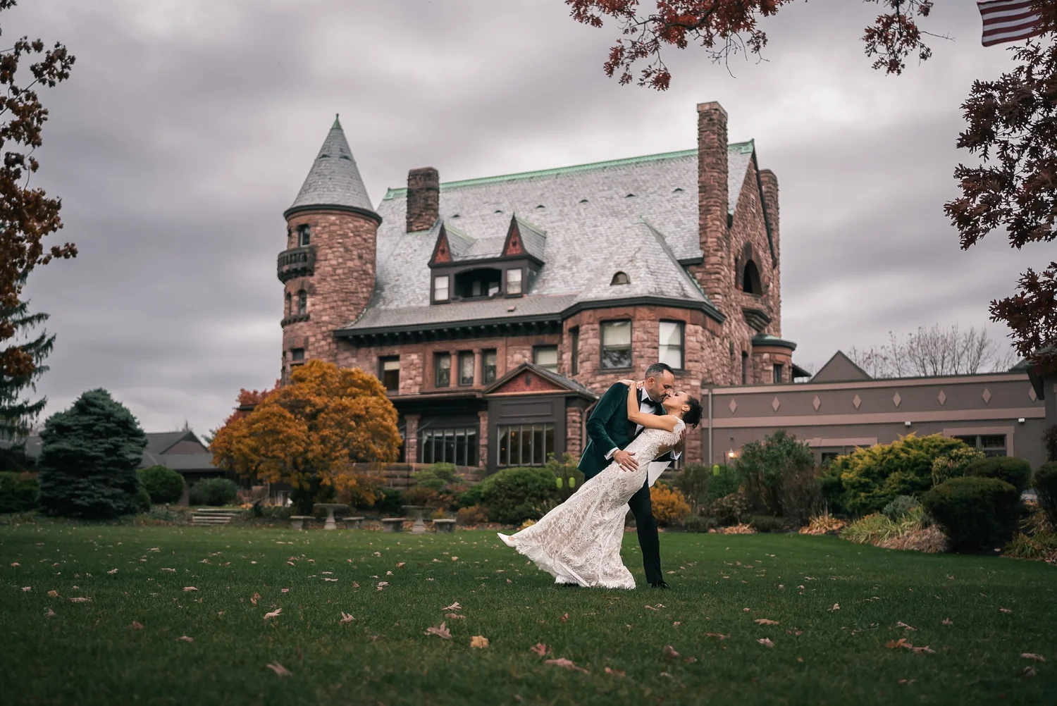 Leon dips Shannon for a kiss on the lawn, with Belhurst Castle and its turret rising behind them on a gray November day