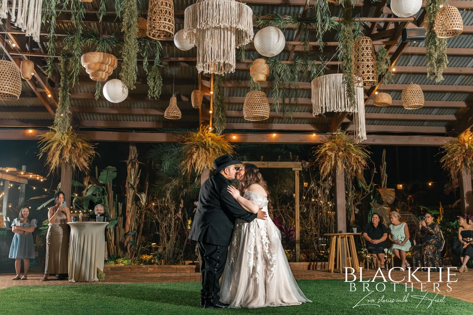 Alyssa and Alberto share their first dance beneath hanging woven lanterns and greenery as guests look on.