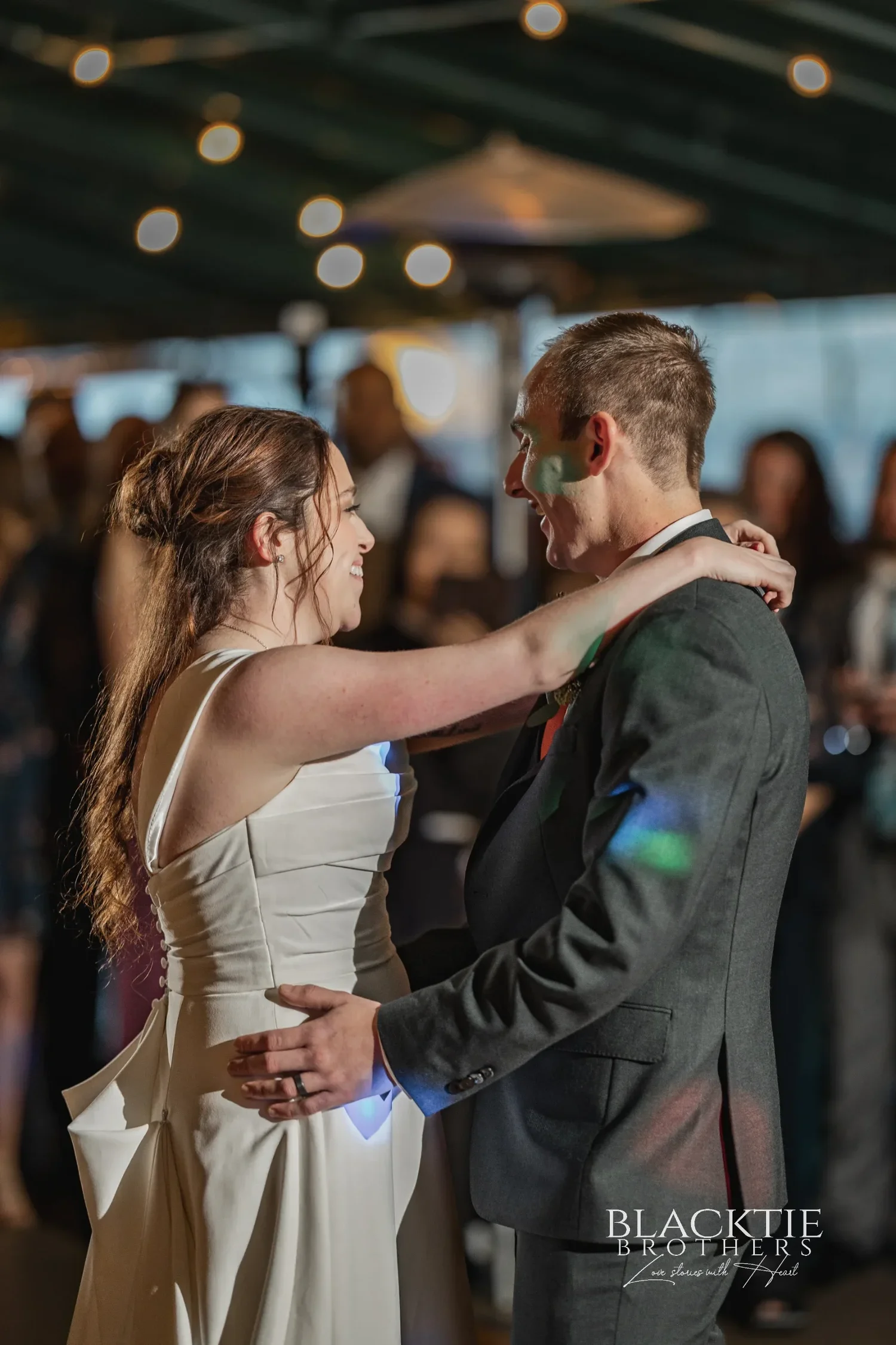 Anya and Gabe's first dance under string lights at Glenora, guests watching from the edge of the floor