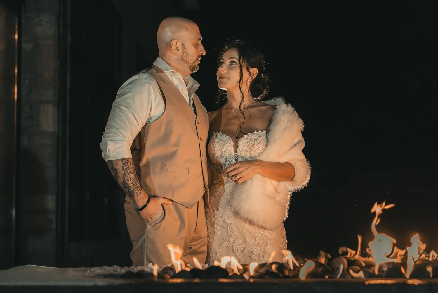 Jill and Nick standing together beside the outdoor fireplace at The Sinclair of Skaneateles after dark