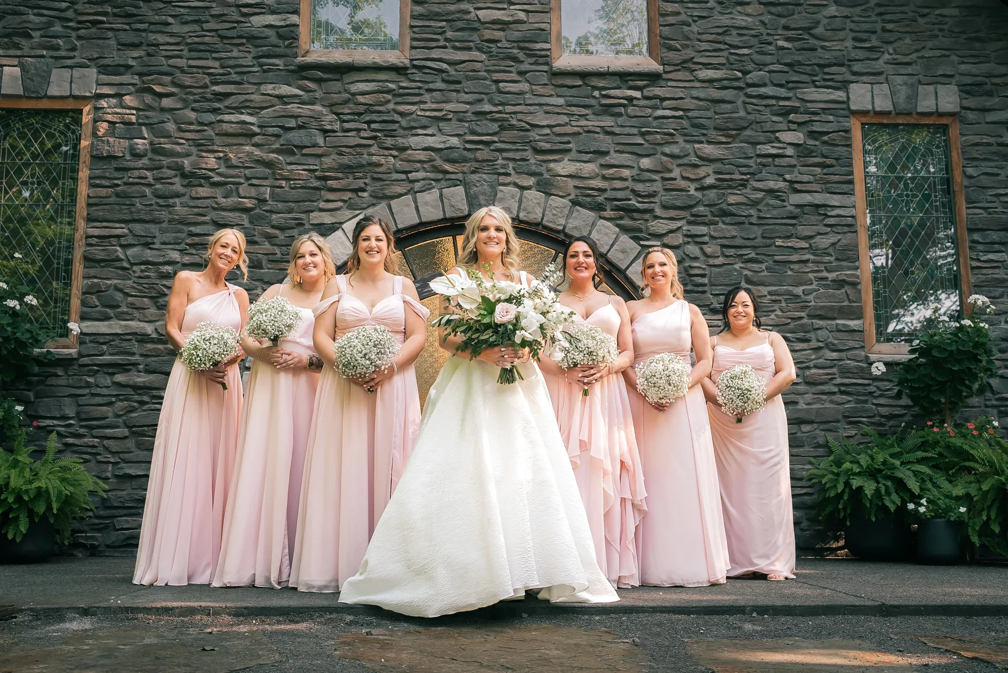 Bride and her bridesmaids in front of the stone Chapel in the Woods at Graceful Gatherings at LedgeRock.