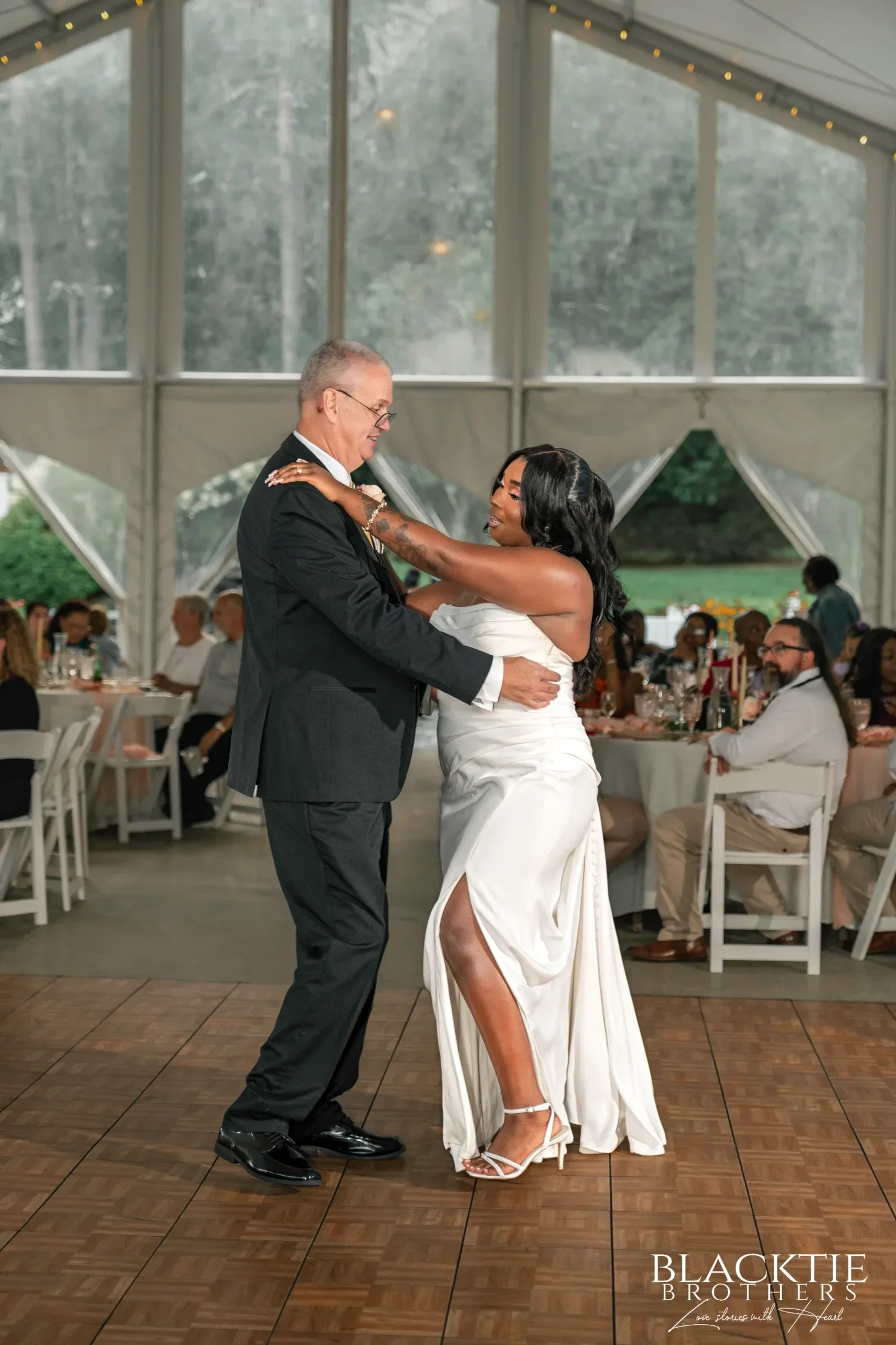 A bride dancing with her father inside the reception tent at Traditions at the Glen while guests watch from their tables