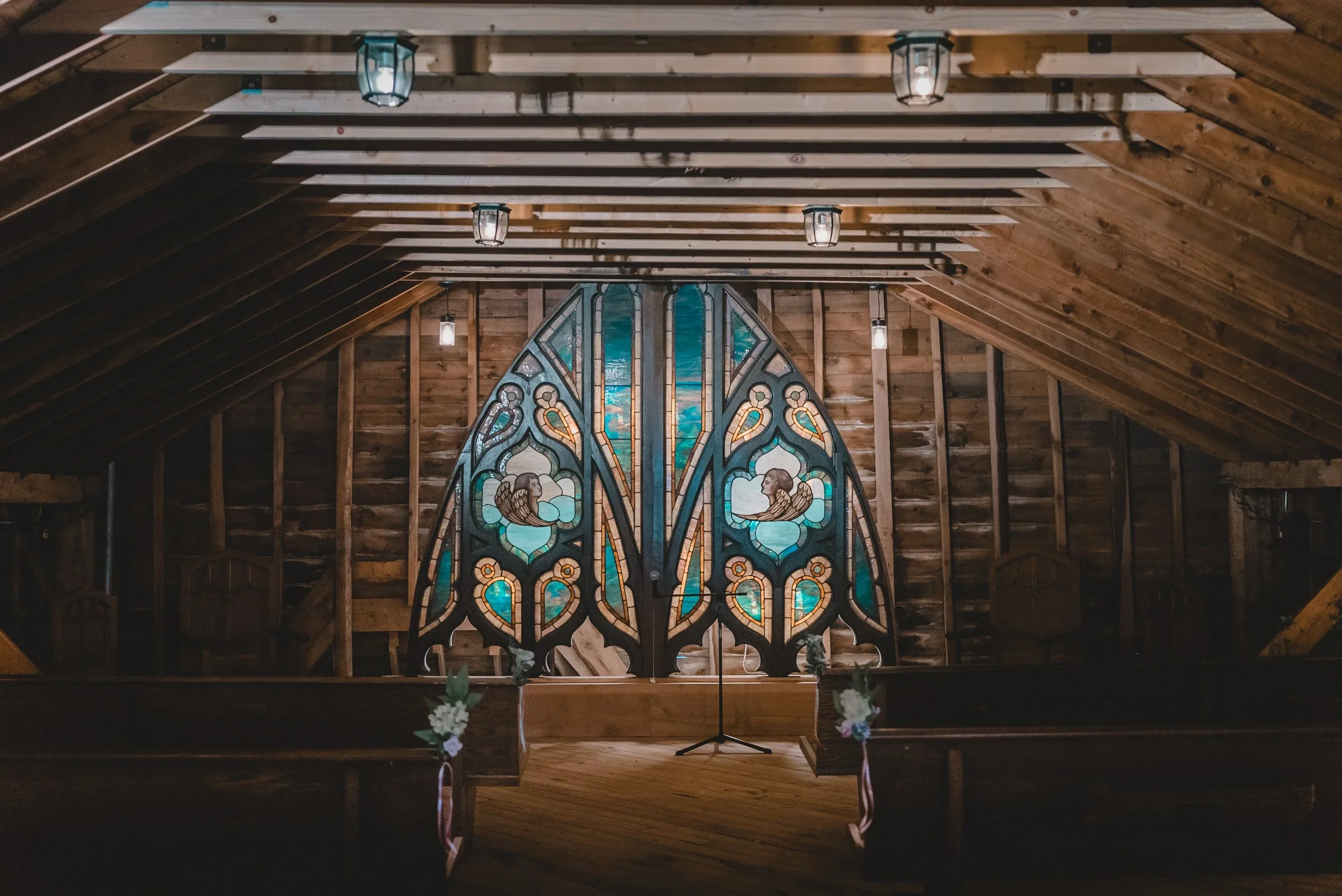 The empty Loft Chapel at Knotting Hill Farm, a timber barn loft with wooden pews and a tall stained glass window behind the altar