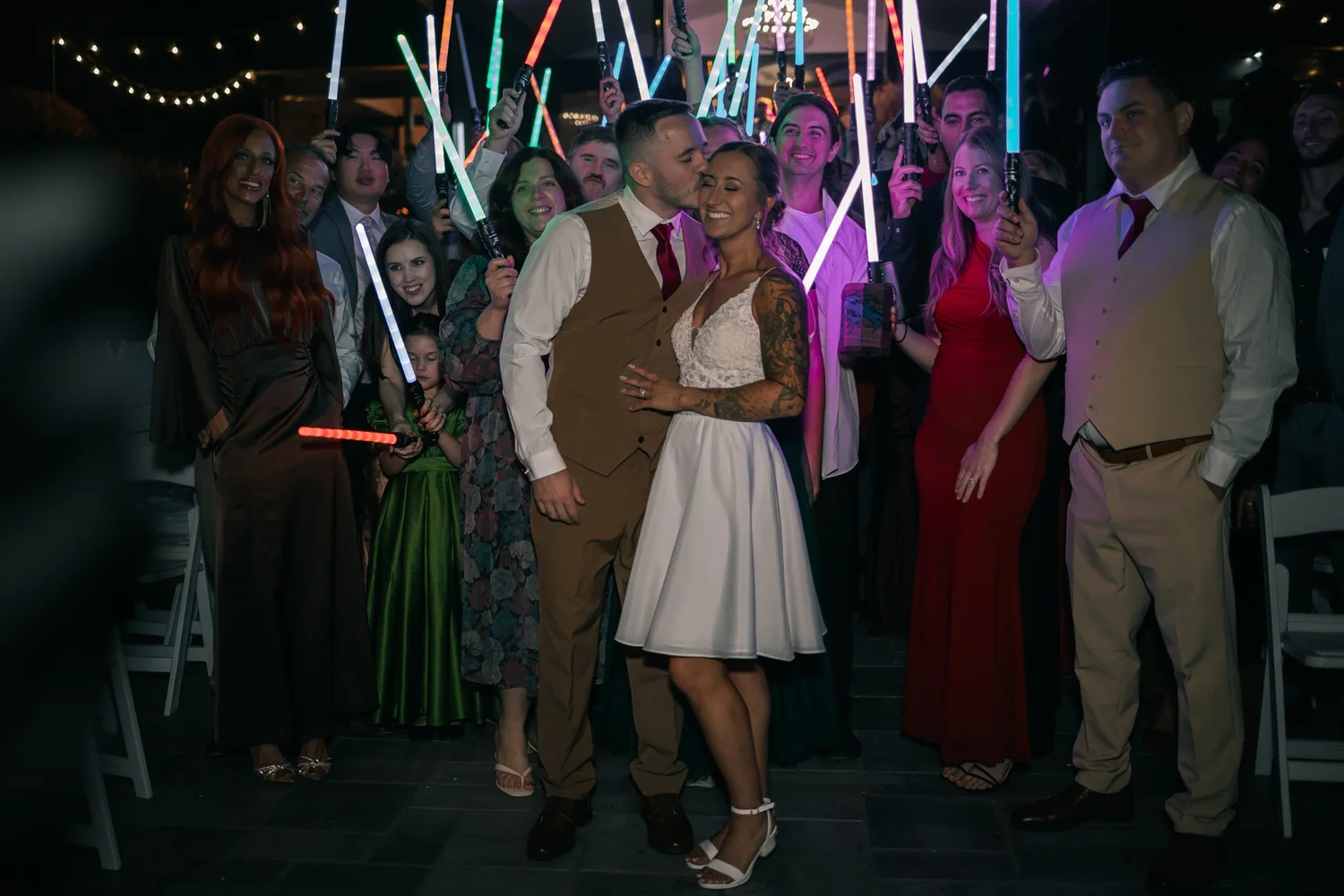Guests waving glowing light sabers on the dark dance floor around Heather and Vincent
