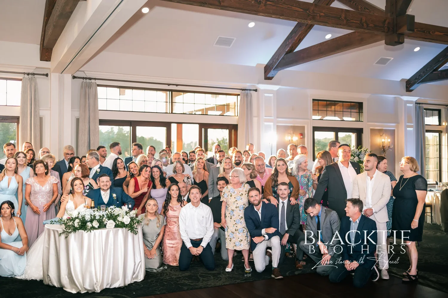 Every guest at Taylor and Jake's wedding gathered around the couple in the ballroom for one group photograph, the trusses and windows behind them