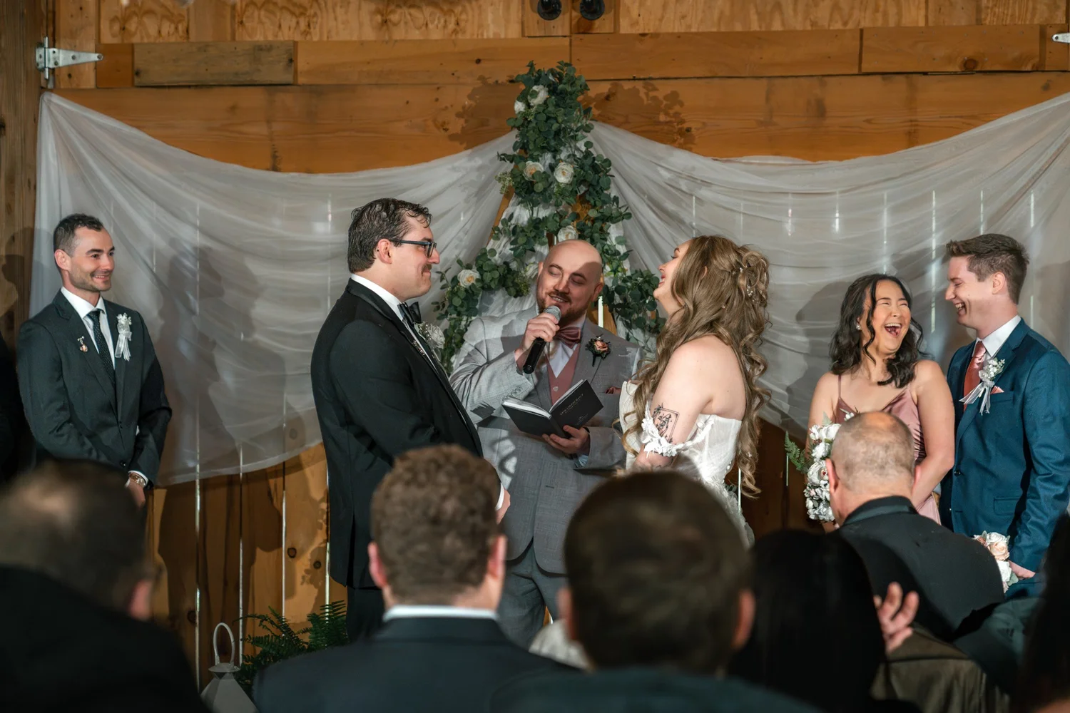 Lindsey laughing during the vows while Noah, the officiant and the wedding party smile