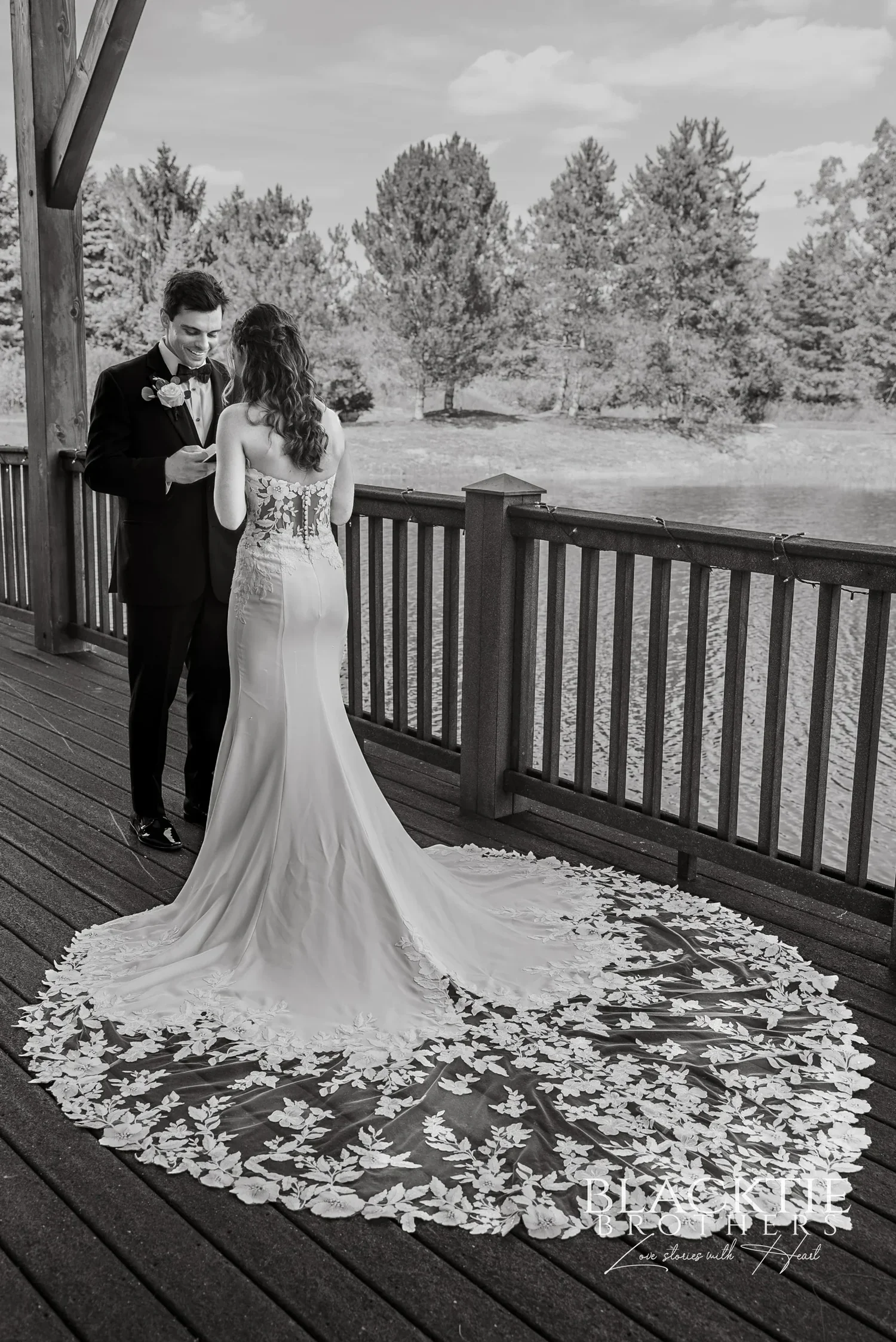 A bride and groom on the deck at Allyn Lodge, her lace train spread across the boards, in black and white.