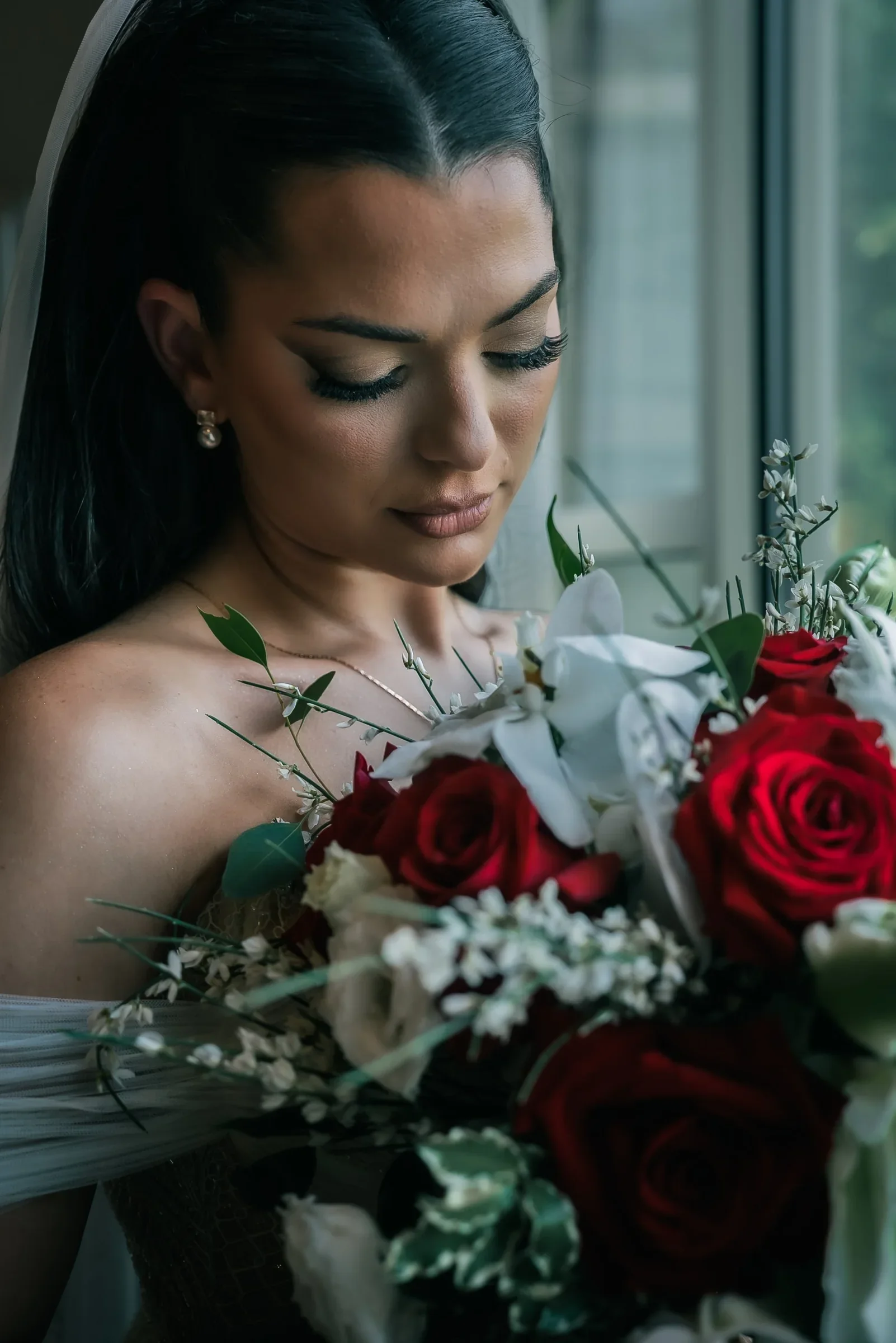 Close portrait of Vanessa looking down at her red rose and white orchid bouquet