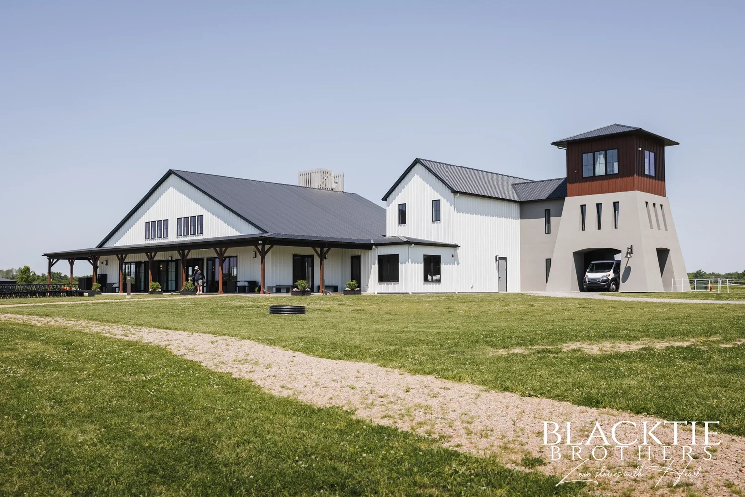The Sally Port View event center from the lawn on a clear day: a white building with a long covered porch, and the stucco viewing tower with an arched opening at its base