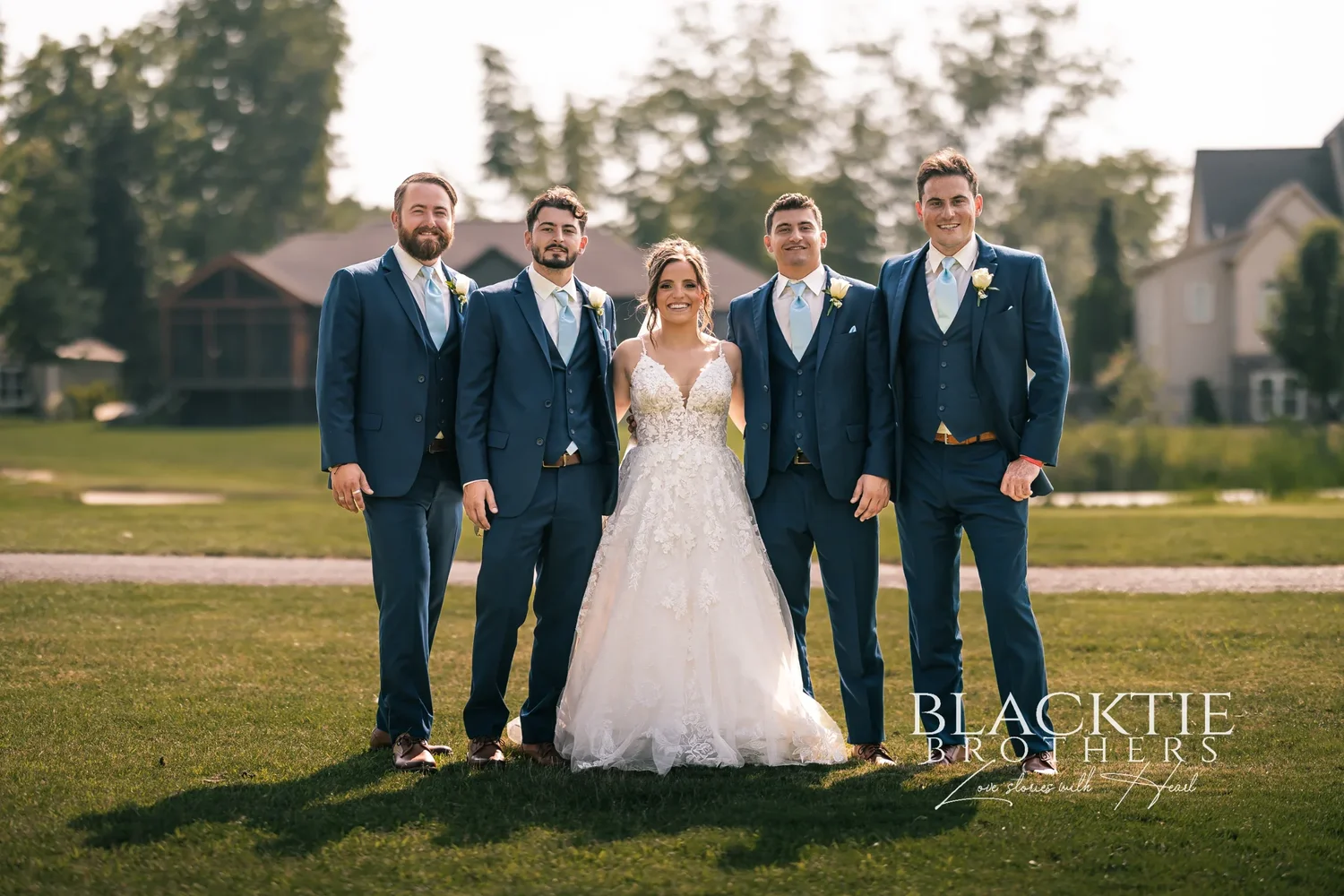 Taylor in her lace gown with Jake's four groomsmen in navy suits on the course at Timber Banks, houses and trees along the fairway behind them