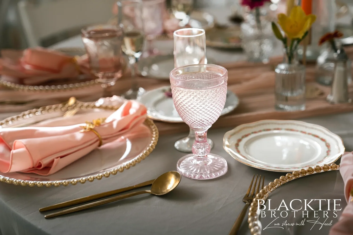 A reception place setting in the tent at Traditions at the Glen with a gold-beaded charger, blush napkin, gold flatware and a pink cut-glass goblet