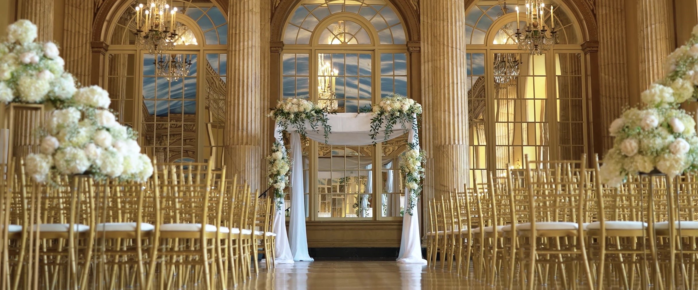Flower arrangements and gold ceremony chairs facing an ornate mirrored wall at Marriott Syracuse Downtown