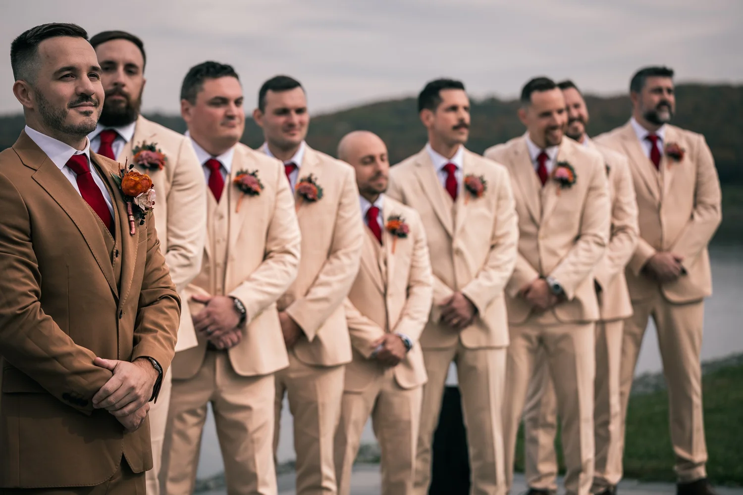 Vincent in a brown suit with his groomsmen in tan suits, lined up on the lawn by the pond