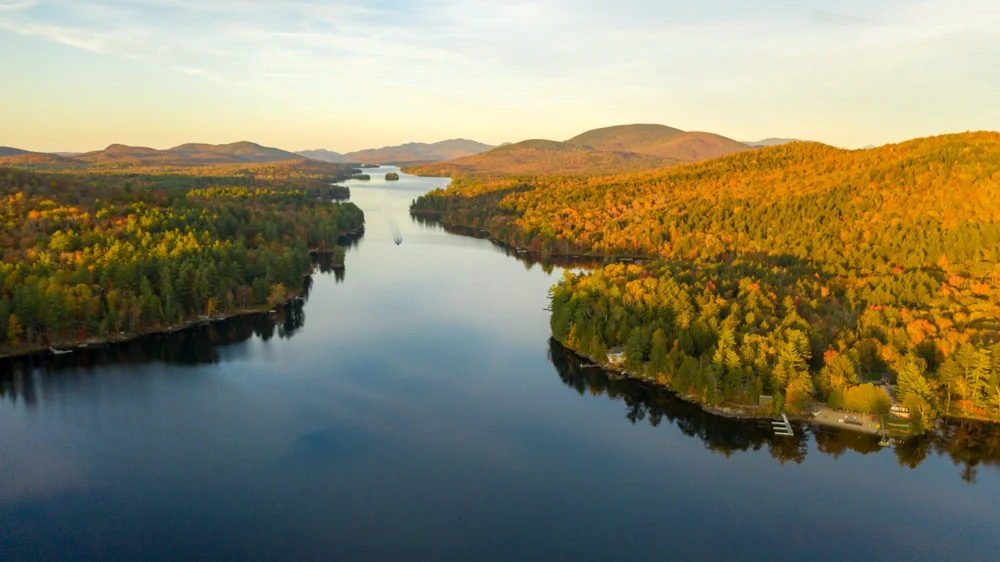 Aerial view over Long Lake in the Adirondacks, with autumn forest and mountains.