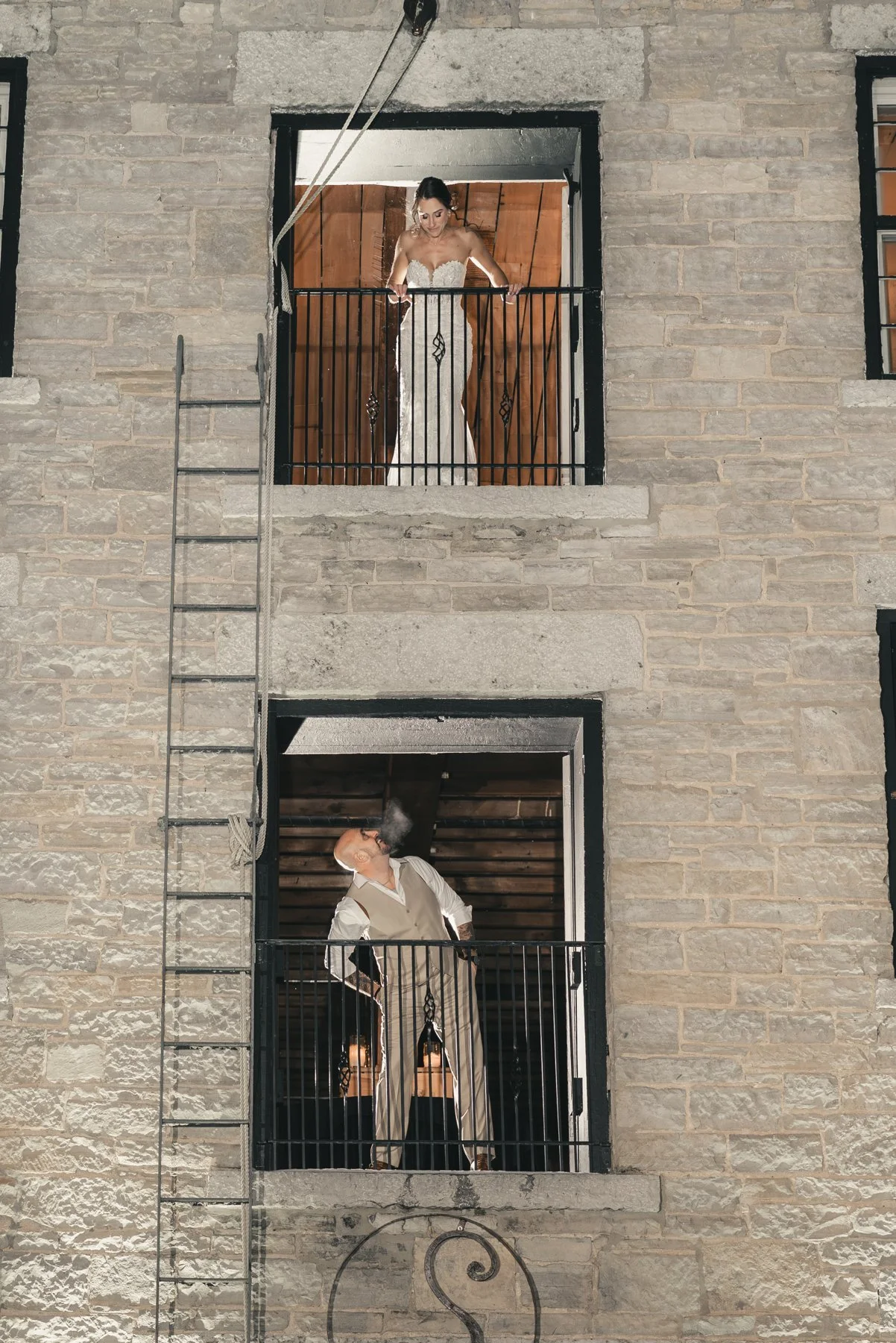 Jill and Nick framed in two upper windows on the stone exterior of The Sinclair of Skaneateles at night
