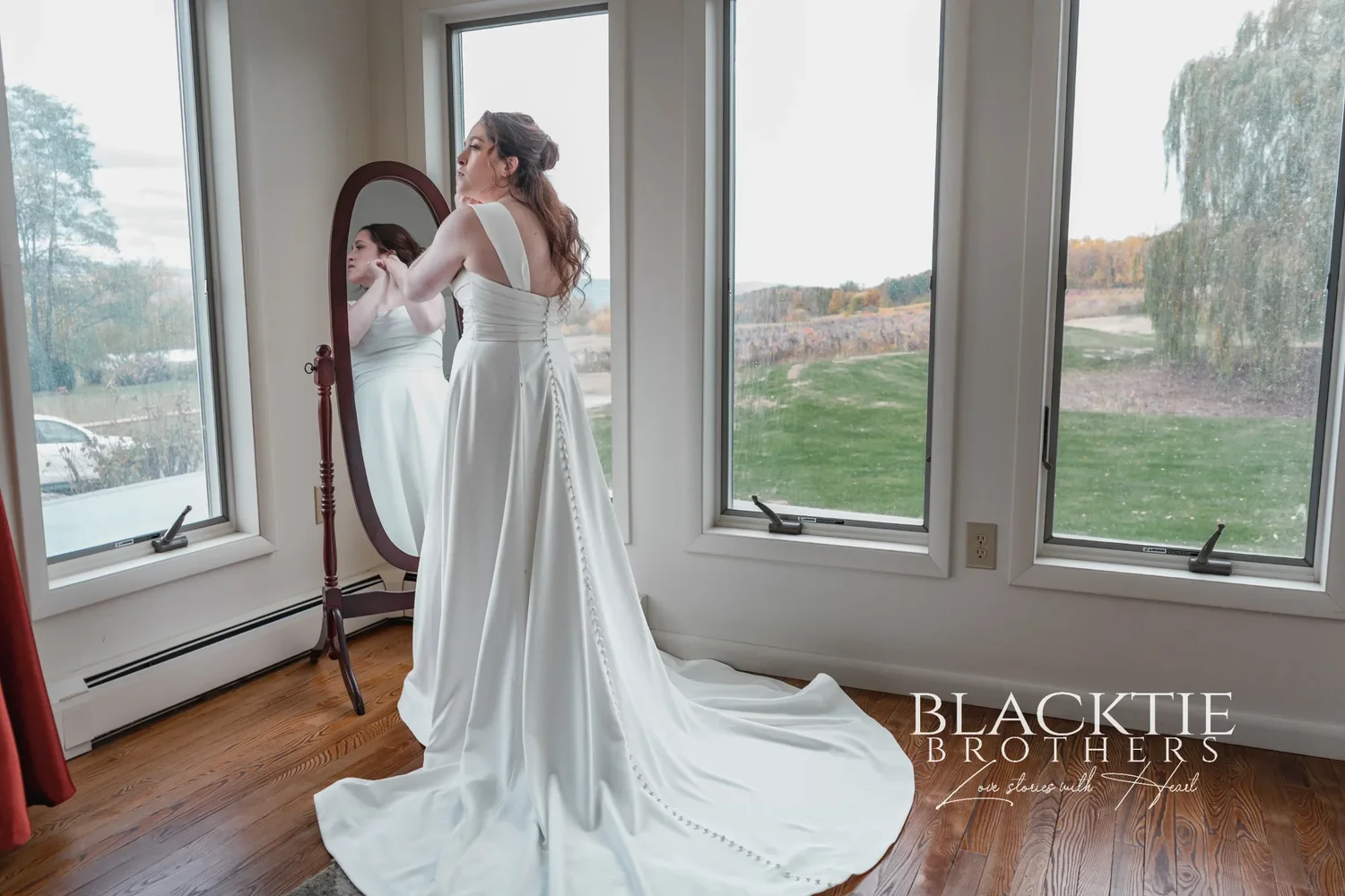 Anya in her wedding dress at a window of the cottage at Glenora, with the grounds and lake view outside