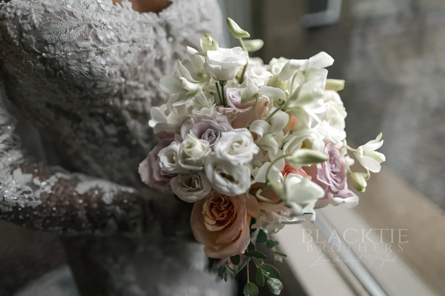 Close-up of the bride’s bouquet of white and blush flowers against the lace of her gown