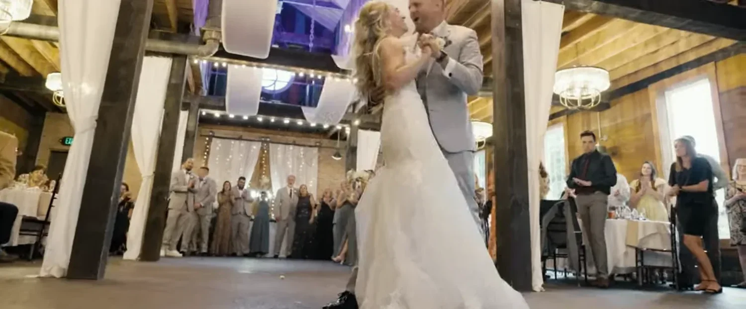 Jennifer and Alex's first dance in the timber-framed reception room at The Cannery, white drapery and string lights above, guests standing around the floor