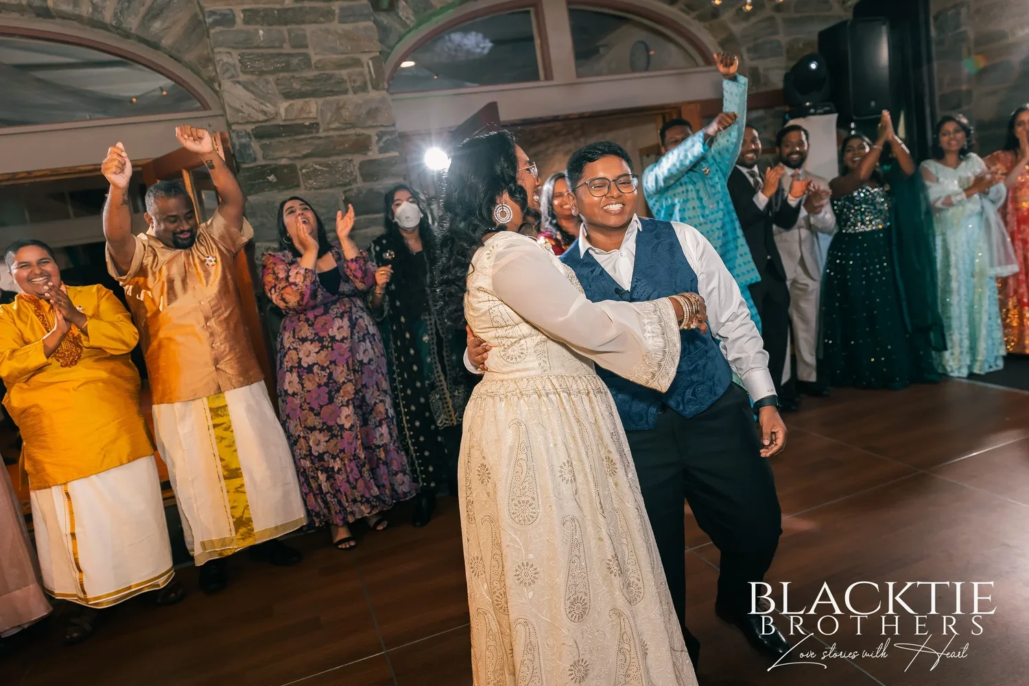 Hima and Alina dancing arm in arm in the middle of the dance floor while guests around them clap and dance