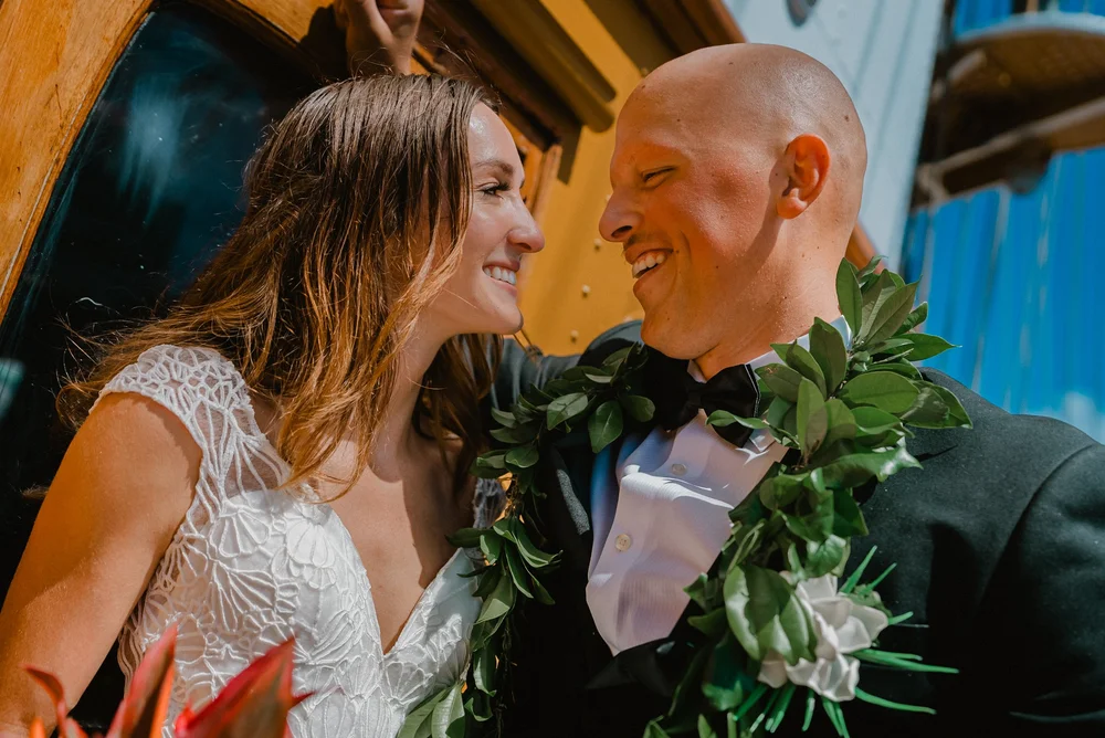 Bride and groom smiling at each other beside the ship’s wooden fittings.