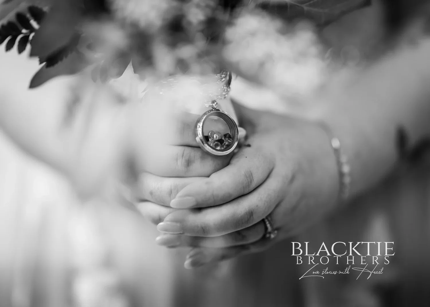Black and white close view of the couple's clasped hands, her engagement ring and wedding band in focus