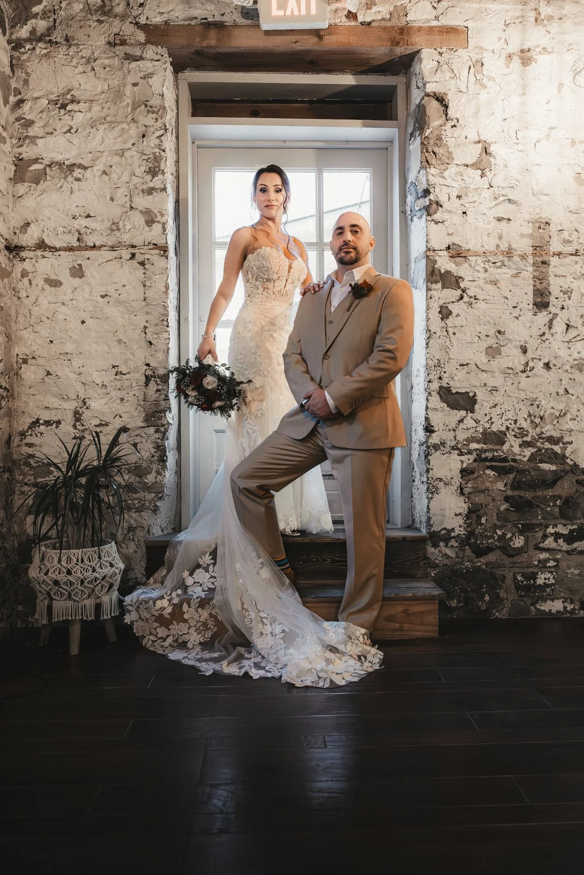 Jill and Nick posing together beside a tall window in a stone-walled room at The Sinclair of Skaneateles