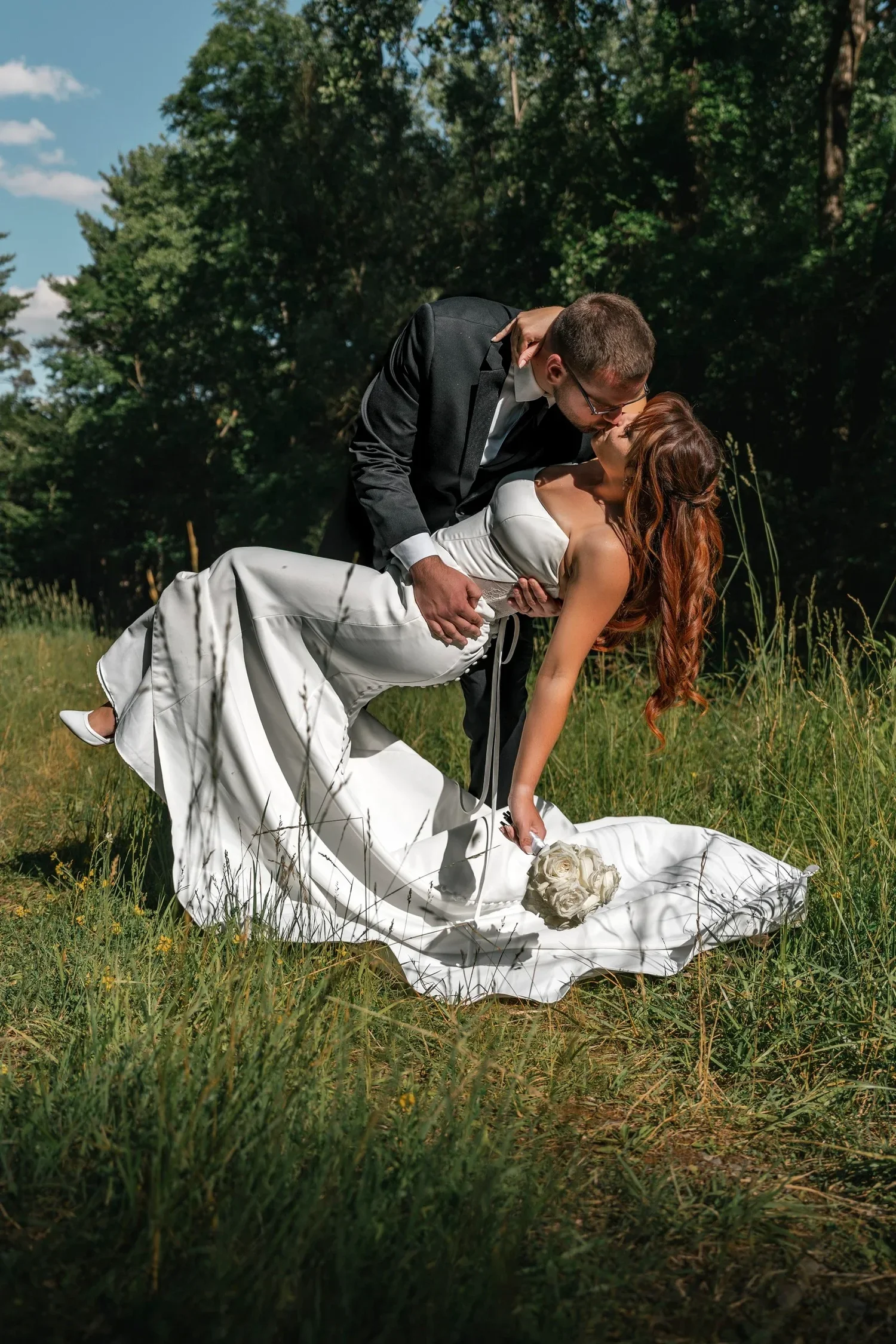 Zach dipping Danielle for a kiss in the tall grass at Traditions at the Glen, her dress spread out around them