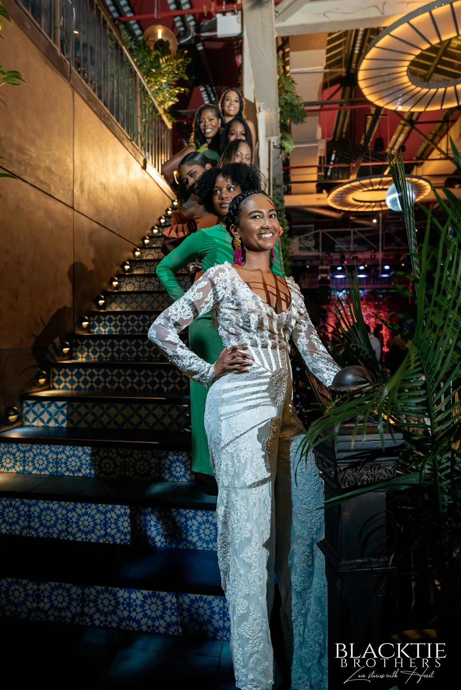 Ciara posing on Fandi Mata's blue and white tiled staircase with a hand on her hip, guests on the steps behind her and the round lamps overhead