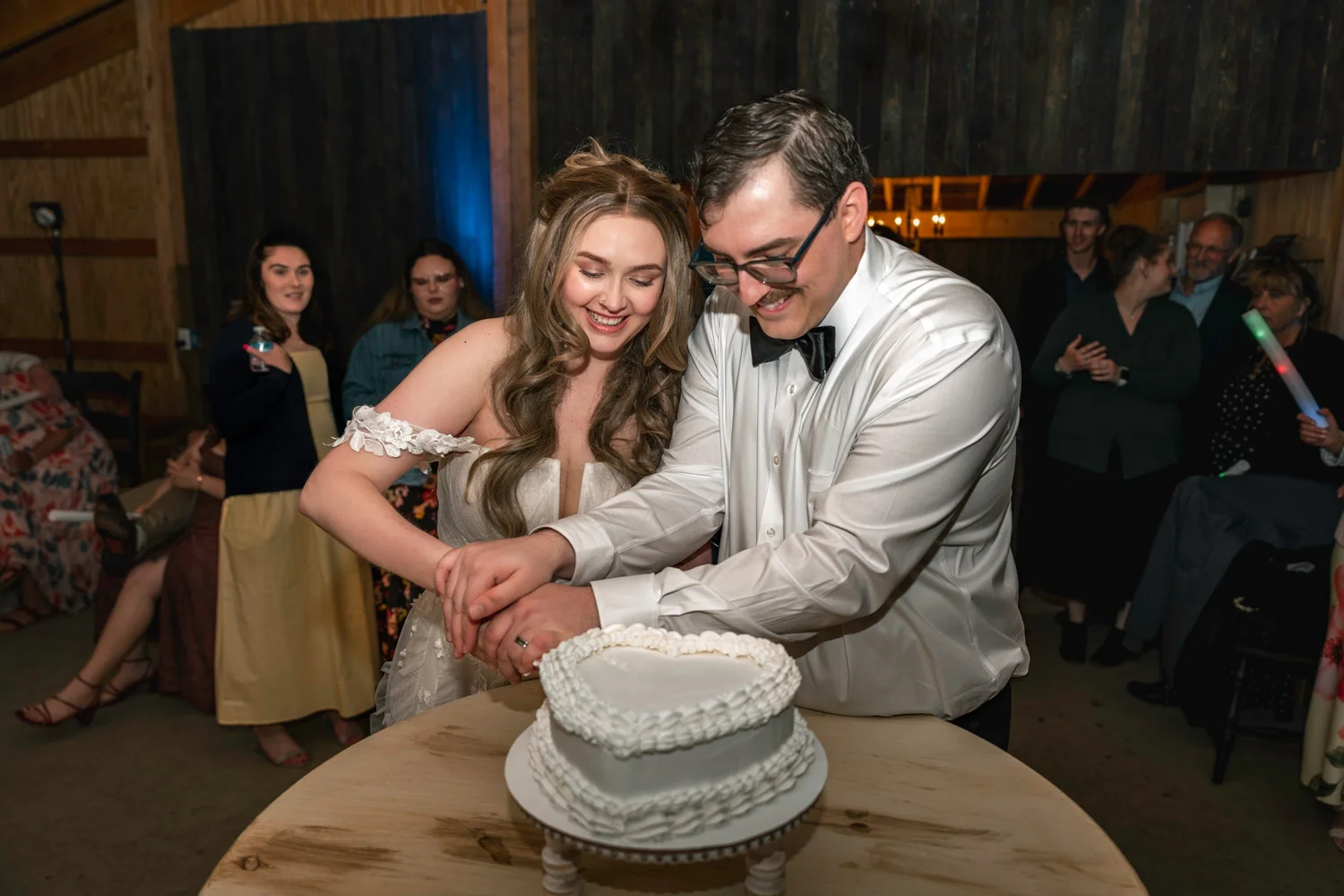 Lindsey and Noah cutting a white wedding cake together, smiling