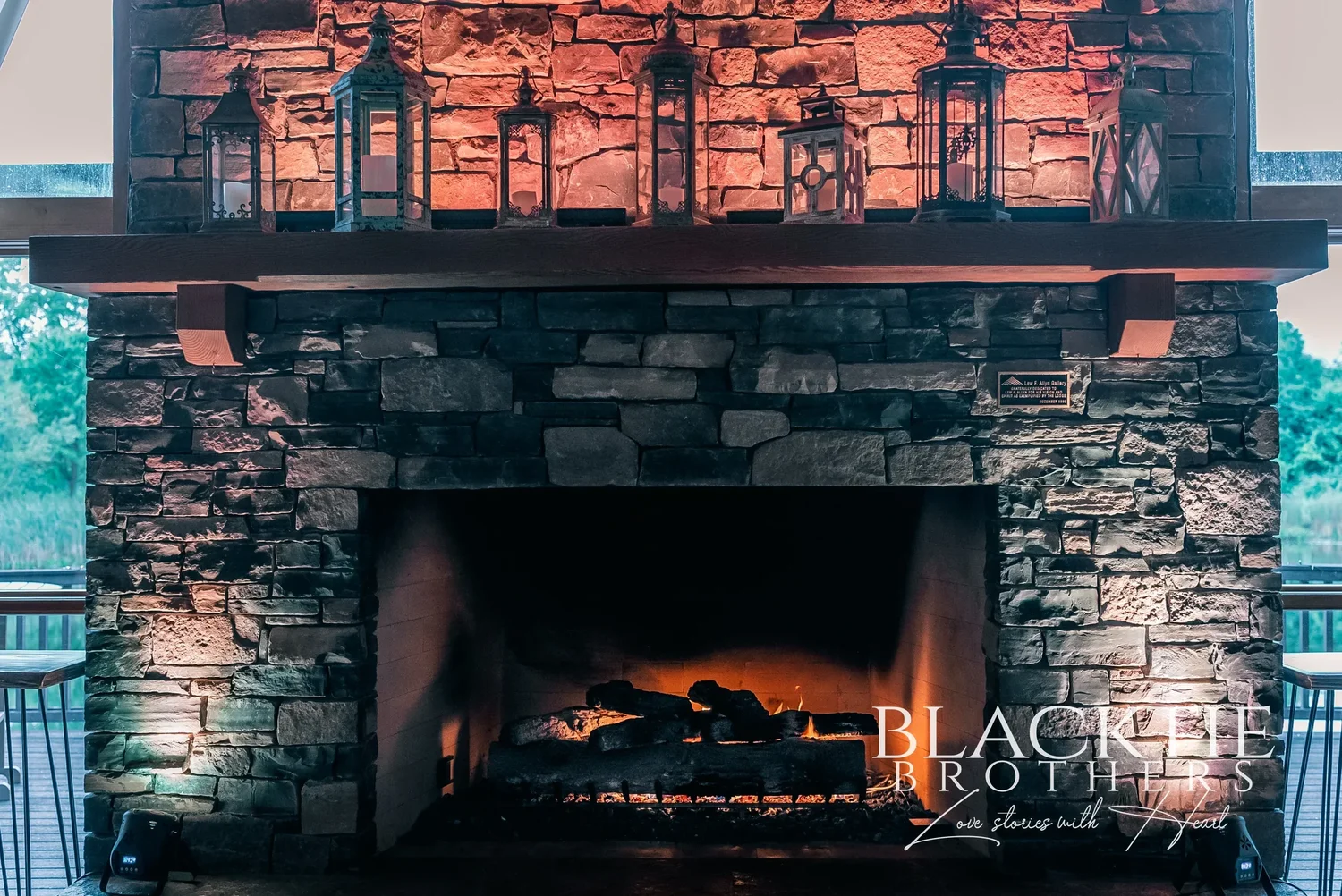 The stone fireplace inside Allyn Lodge, lit, with lanterns along the mantel.