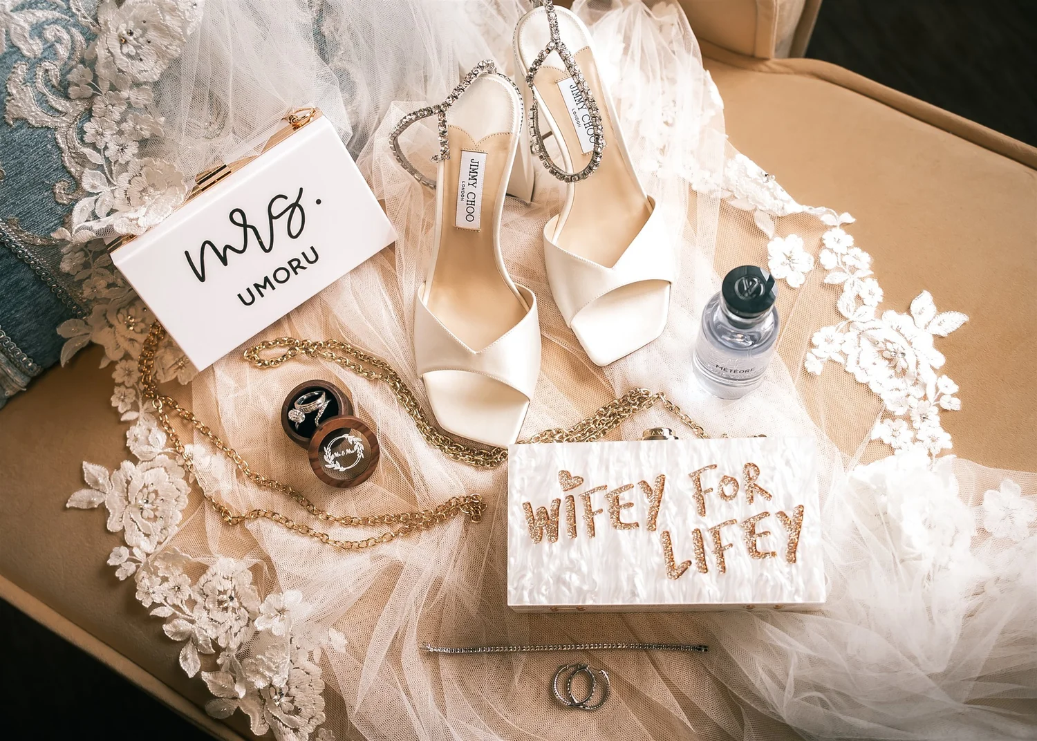 White wedding shoes, rings, perfume and bridal accessories arranged on lace.