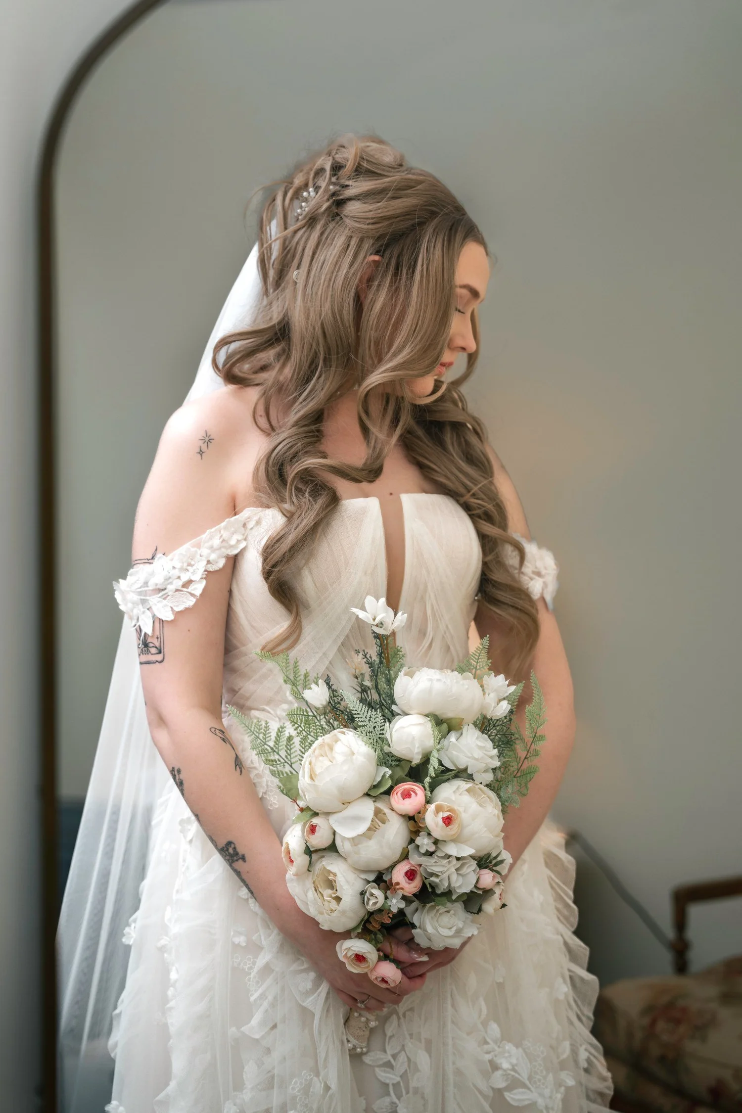 Lindsey in her wedding dress by a bright window, looking down at a bouquet of white flowers